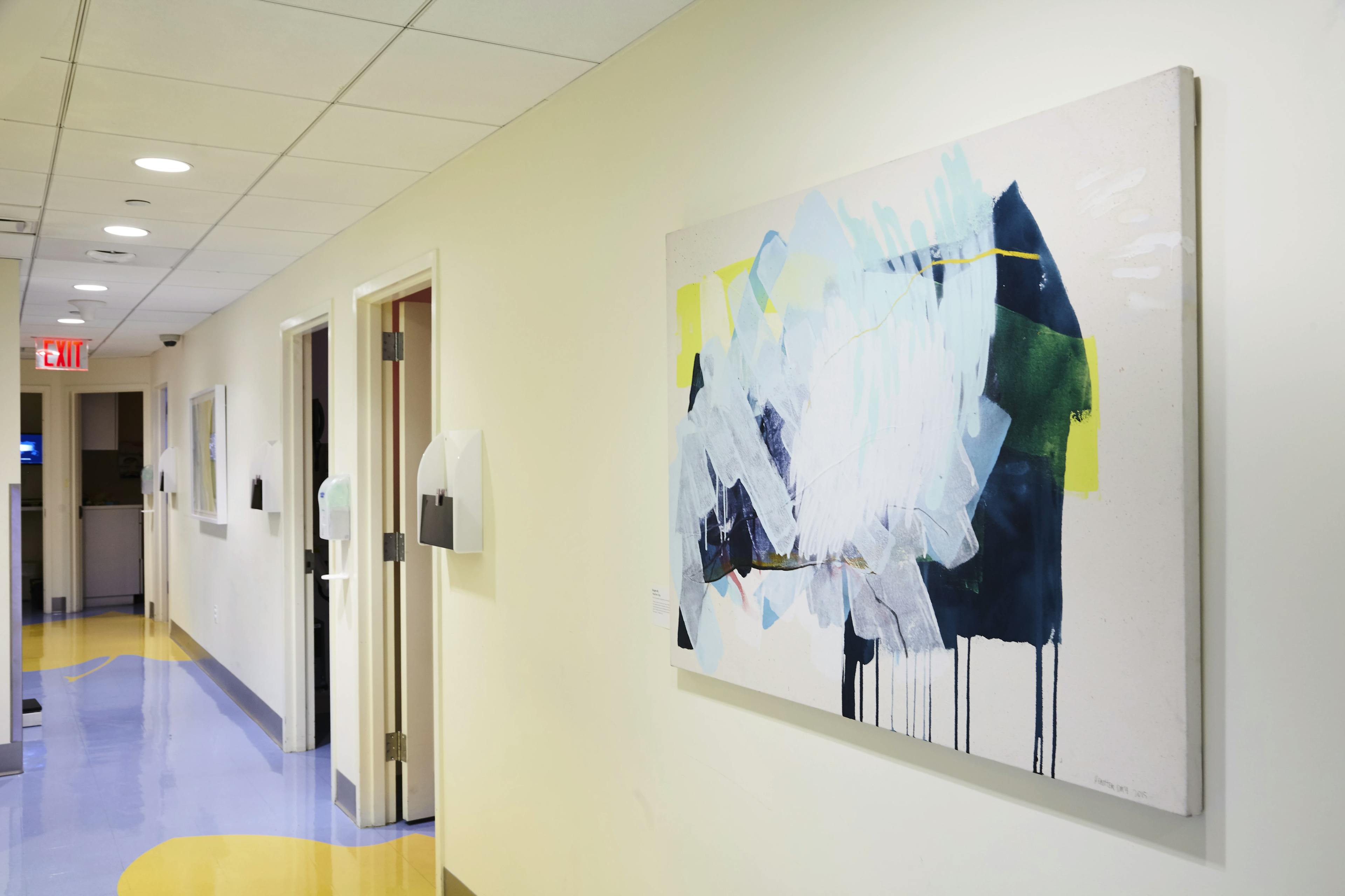 Abstract gestural painting on canvas installed on a beige wall in a hospital corridor.