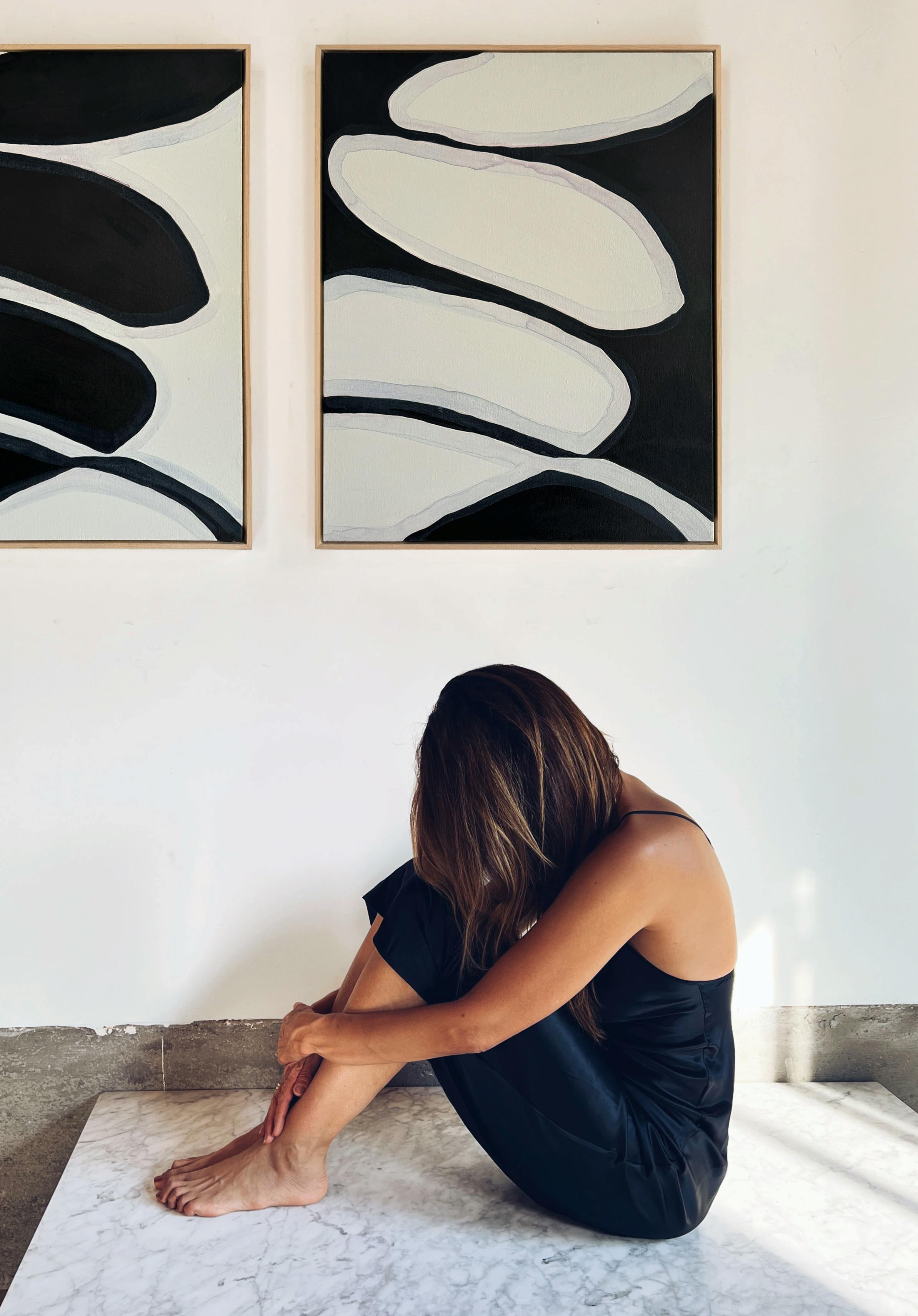 Artist Karina Bania crouched below two black and white abstract floral paintings in her studio.