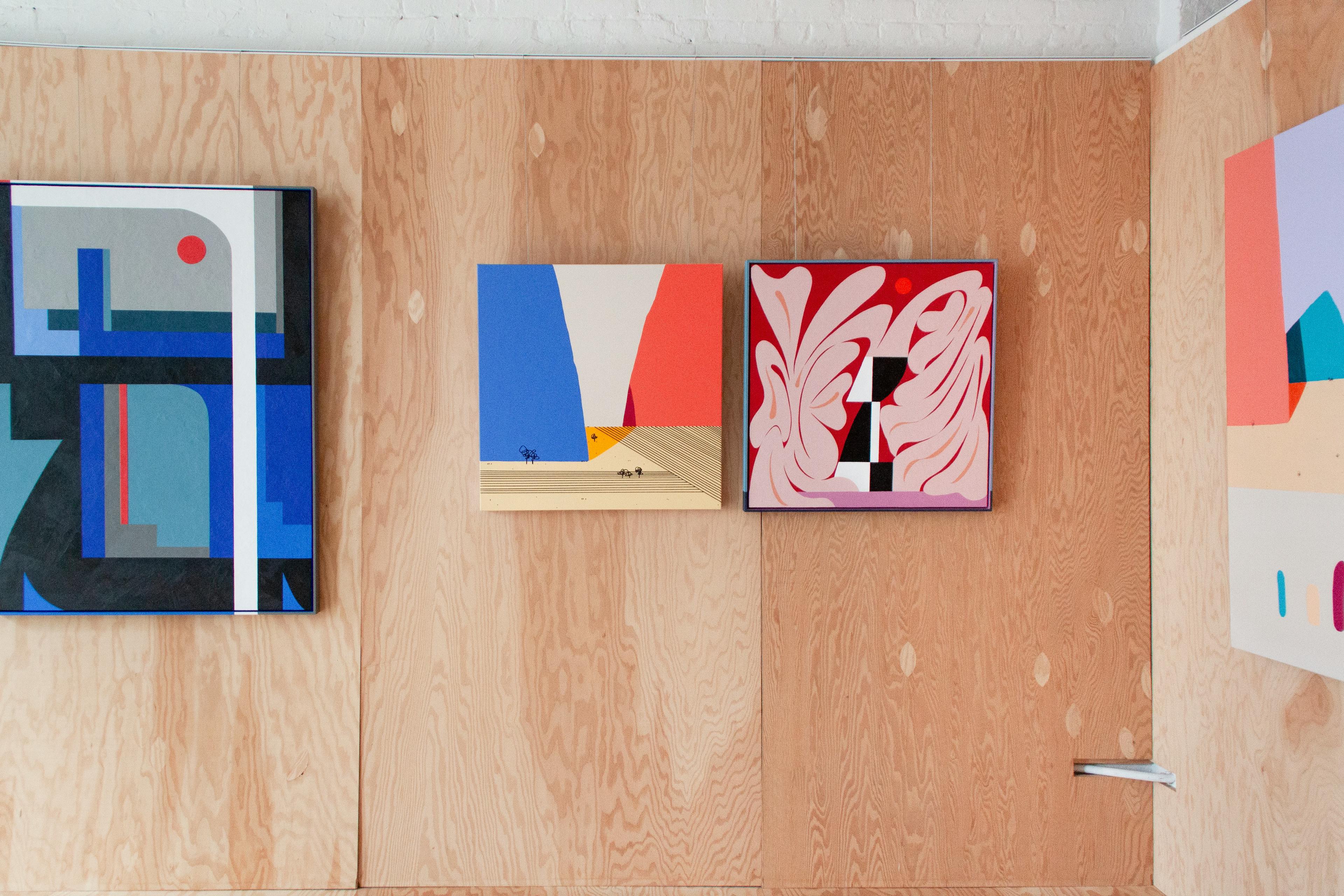 A gallery with wood walls displaying paintings by David Esquivel and Evi O for exhibition Universe, Understood.