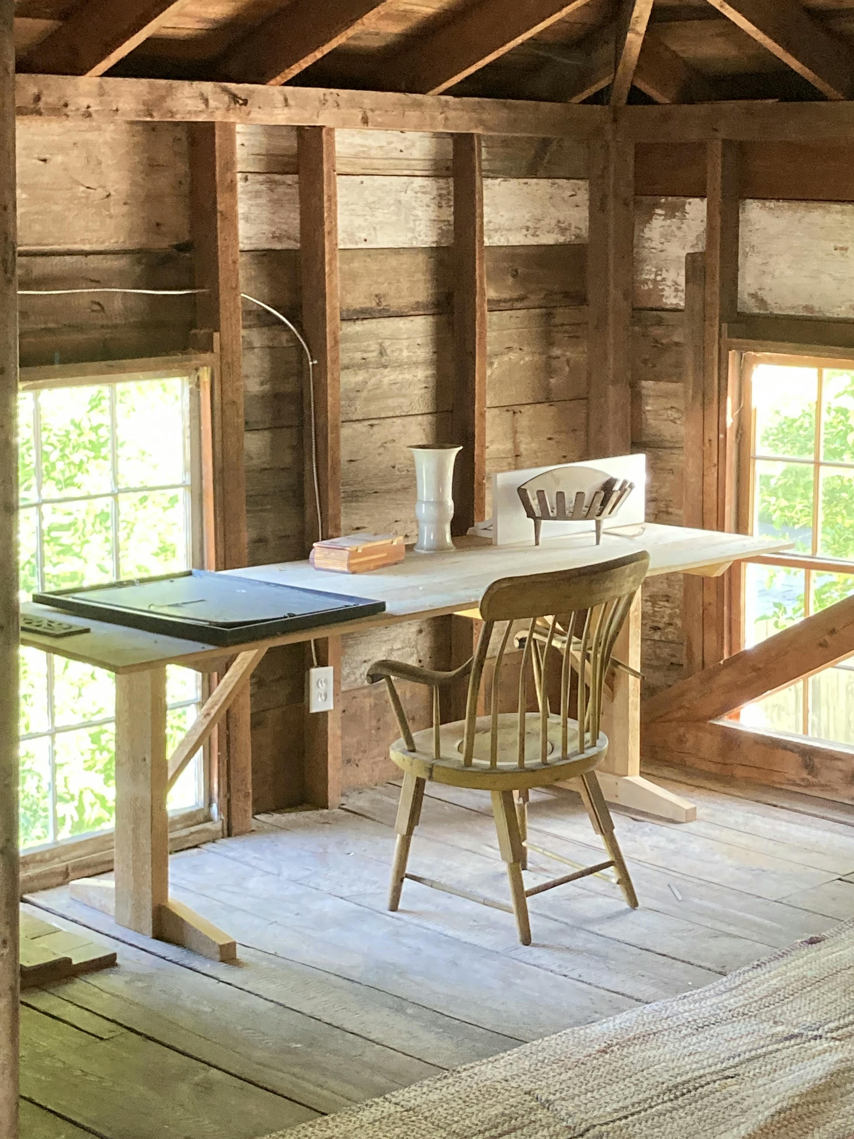 A wooden desk and chair in a sunny, wooden room with two large windows at the Waldoboro Inn in Maine.