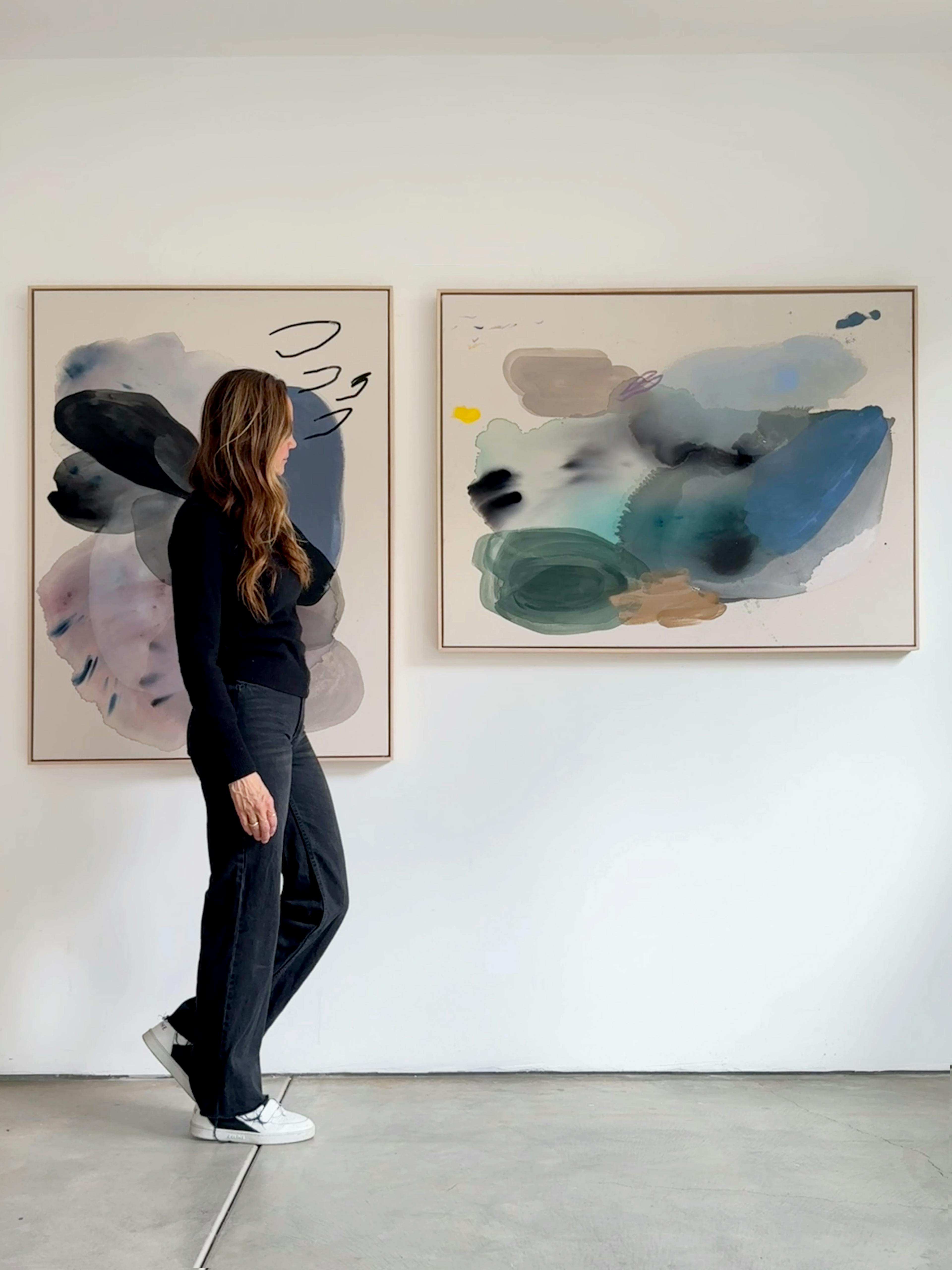 Artist Karina Bania walking in front of two gestural paintings installed on a white wall.