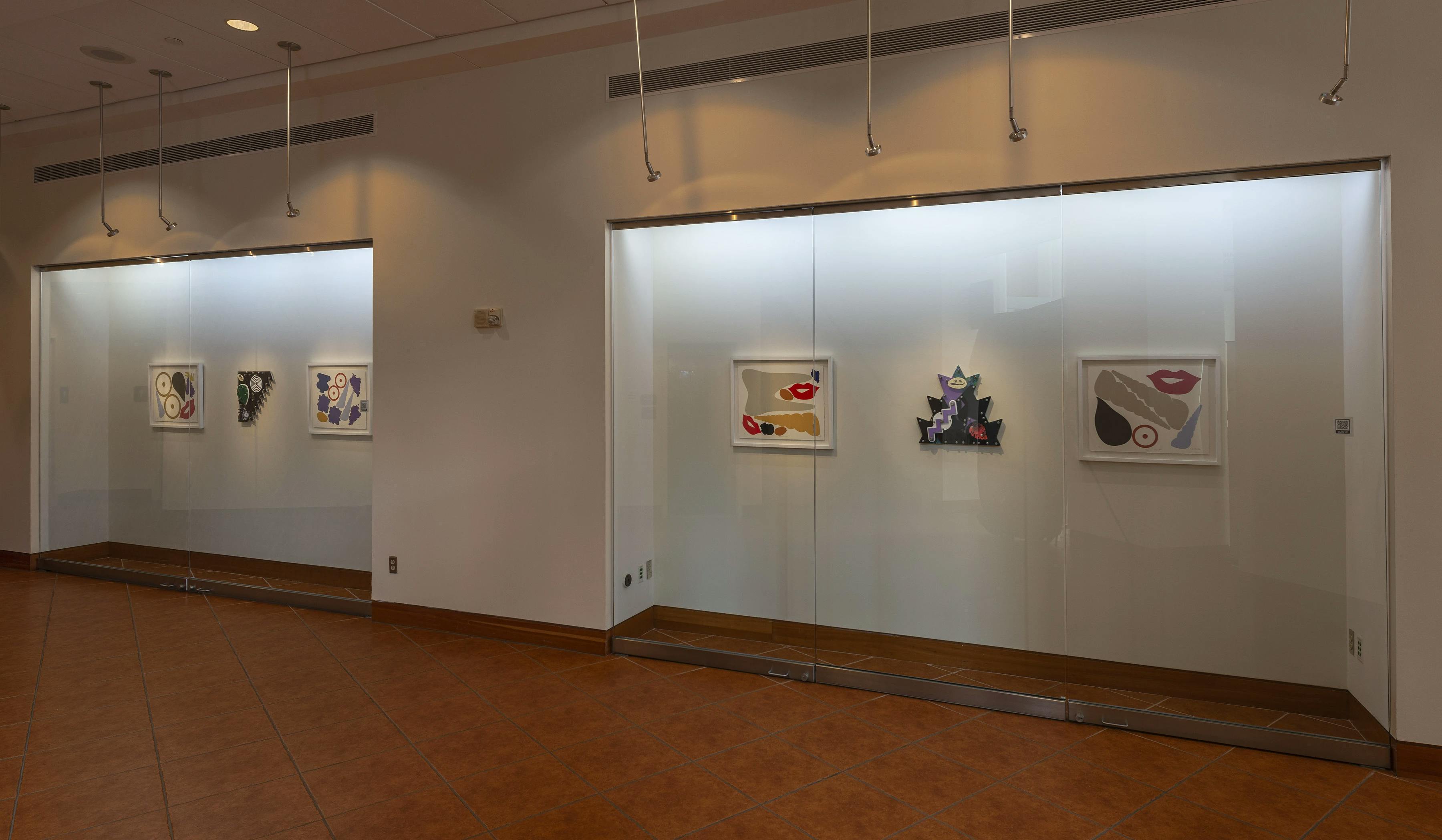 Framed digital prints and abstract sculptures by artist Damien Davis installed in a row behind a glass case at Montclair State University.