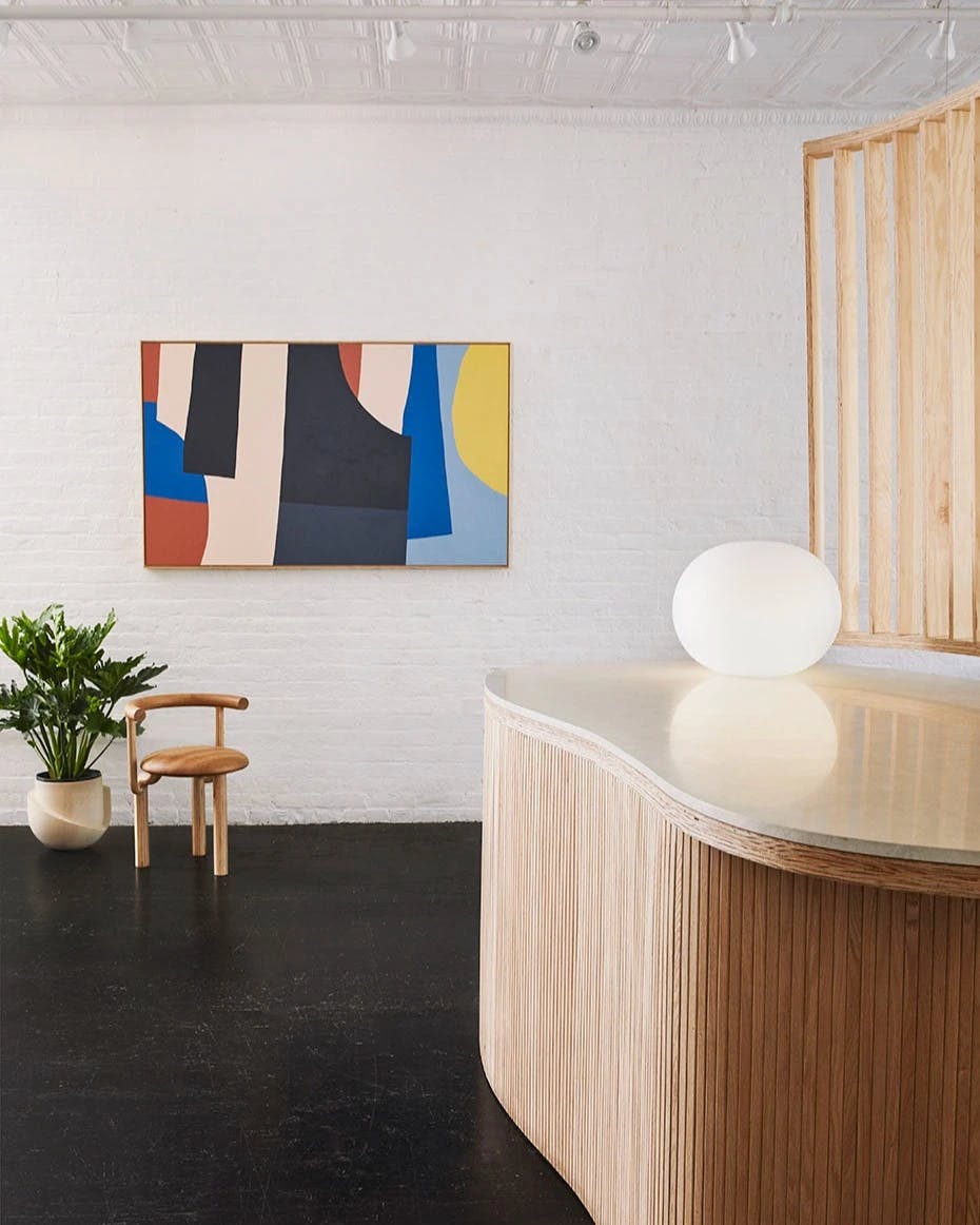 A room with a bean-shaped wood and stone table, orb light, abstract painting on a white wall, and wood chair.