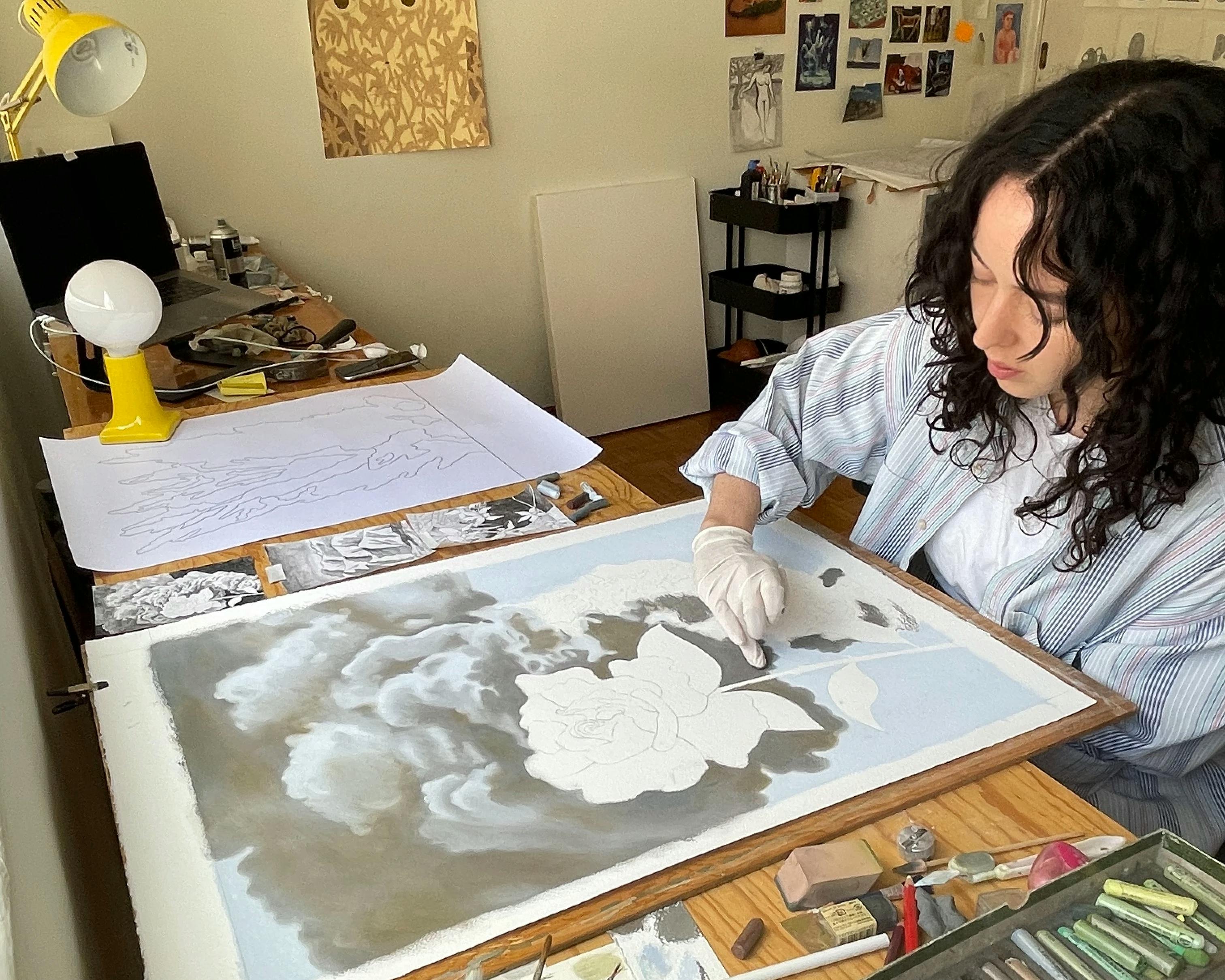 Artist Rachel Levit Ruiz wearing white gloves and smudging charcoal pastel on a drawing of flowers in clouds.