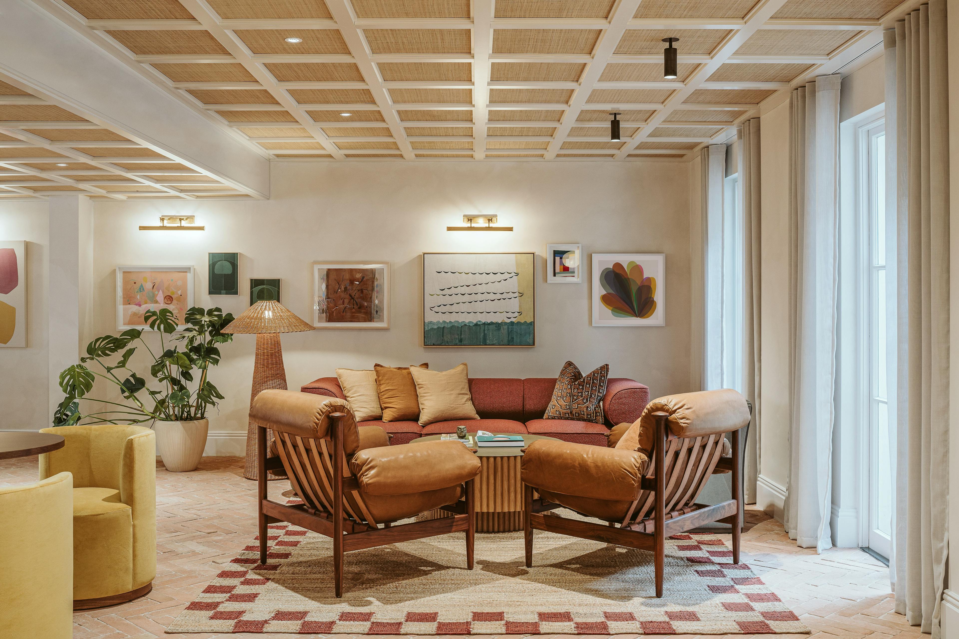 A lounge area at the Chief London clubhouse with artwork by artists Kayla Plosz Antiel, Carla Weeks, Lydia Bassis, Liesl Pfeffer and Laura Berman installed on a white wall above an orange sofa.