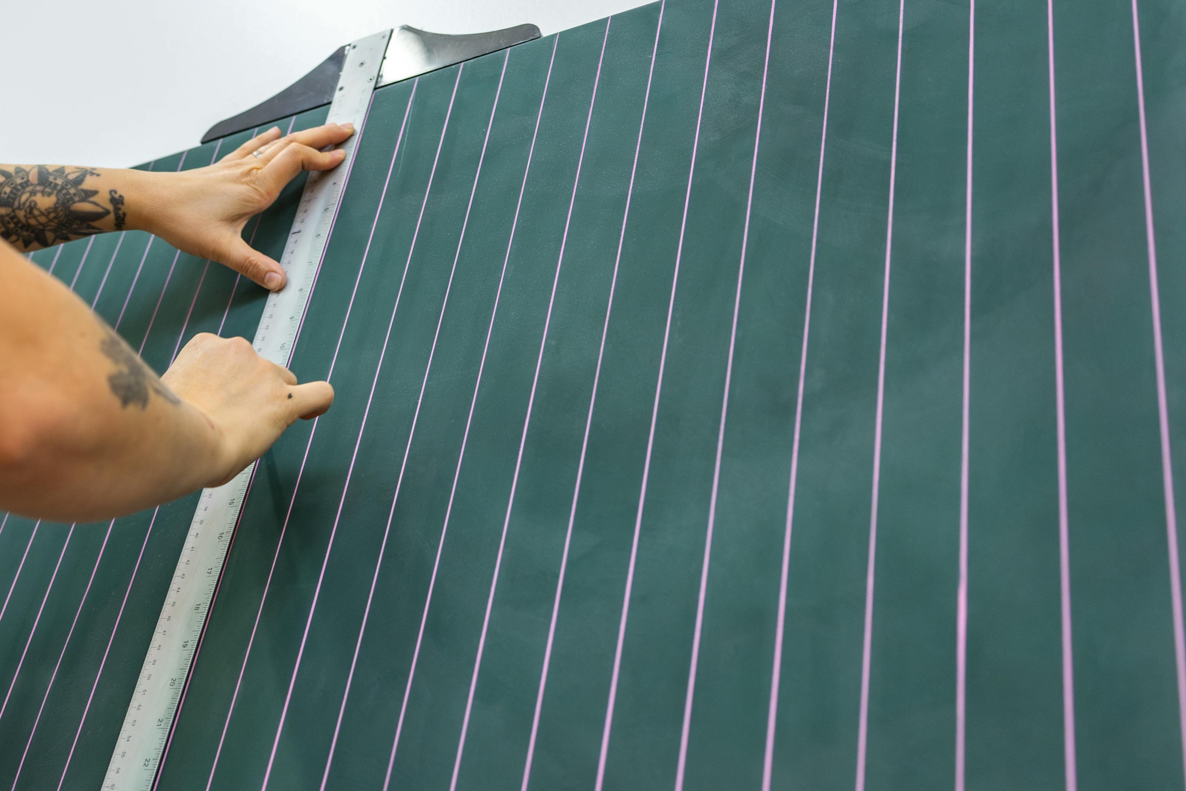 Artist Arielle Zamora using a ruler to create vertical purple lines on a green panel.