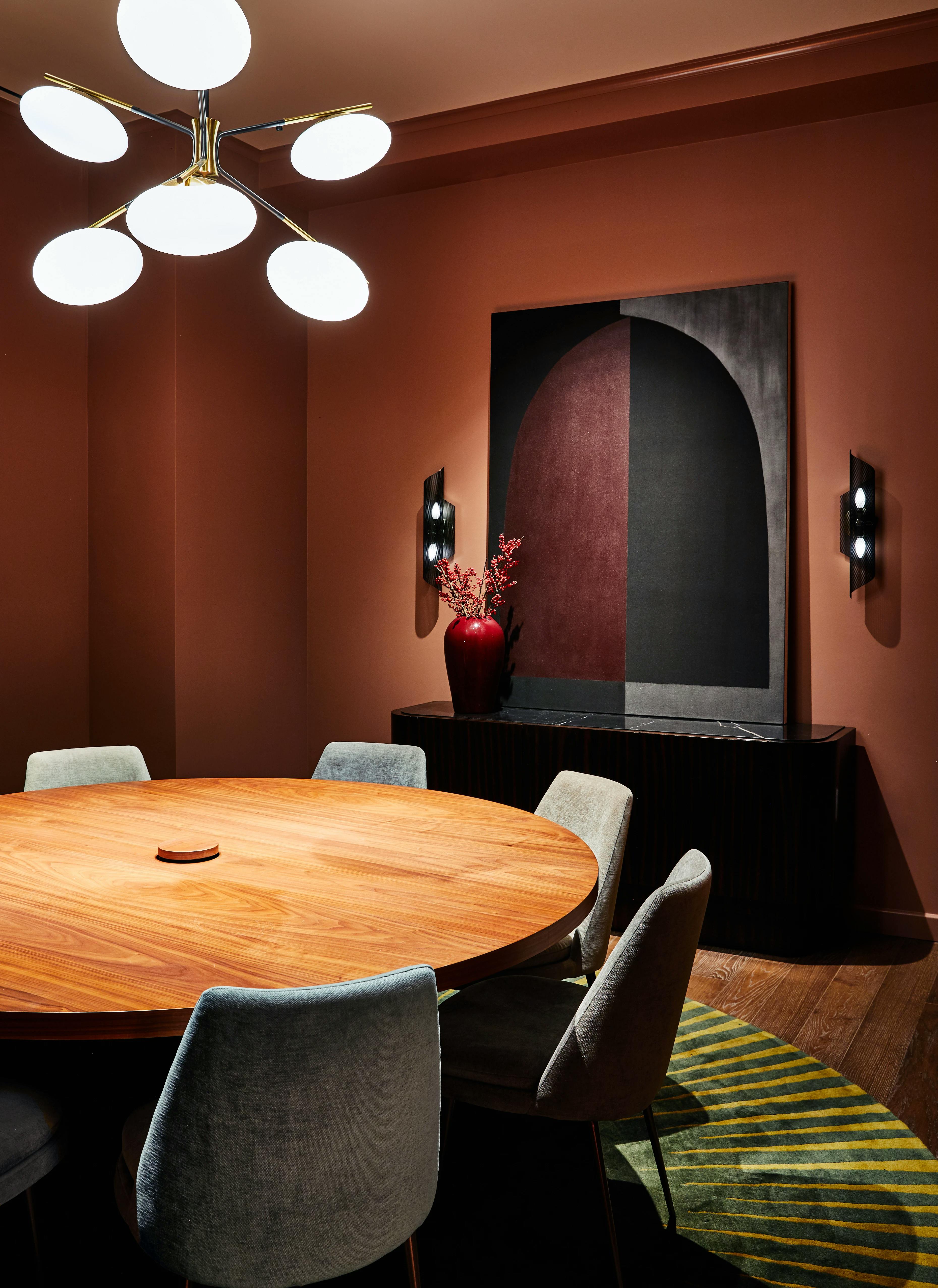 A conference room at the Chief Flatiron Clubhouse with a circular wooden table and a geometric red and black painting with an arch by artist Aschely Vaughan Cone installed on a red wall.