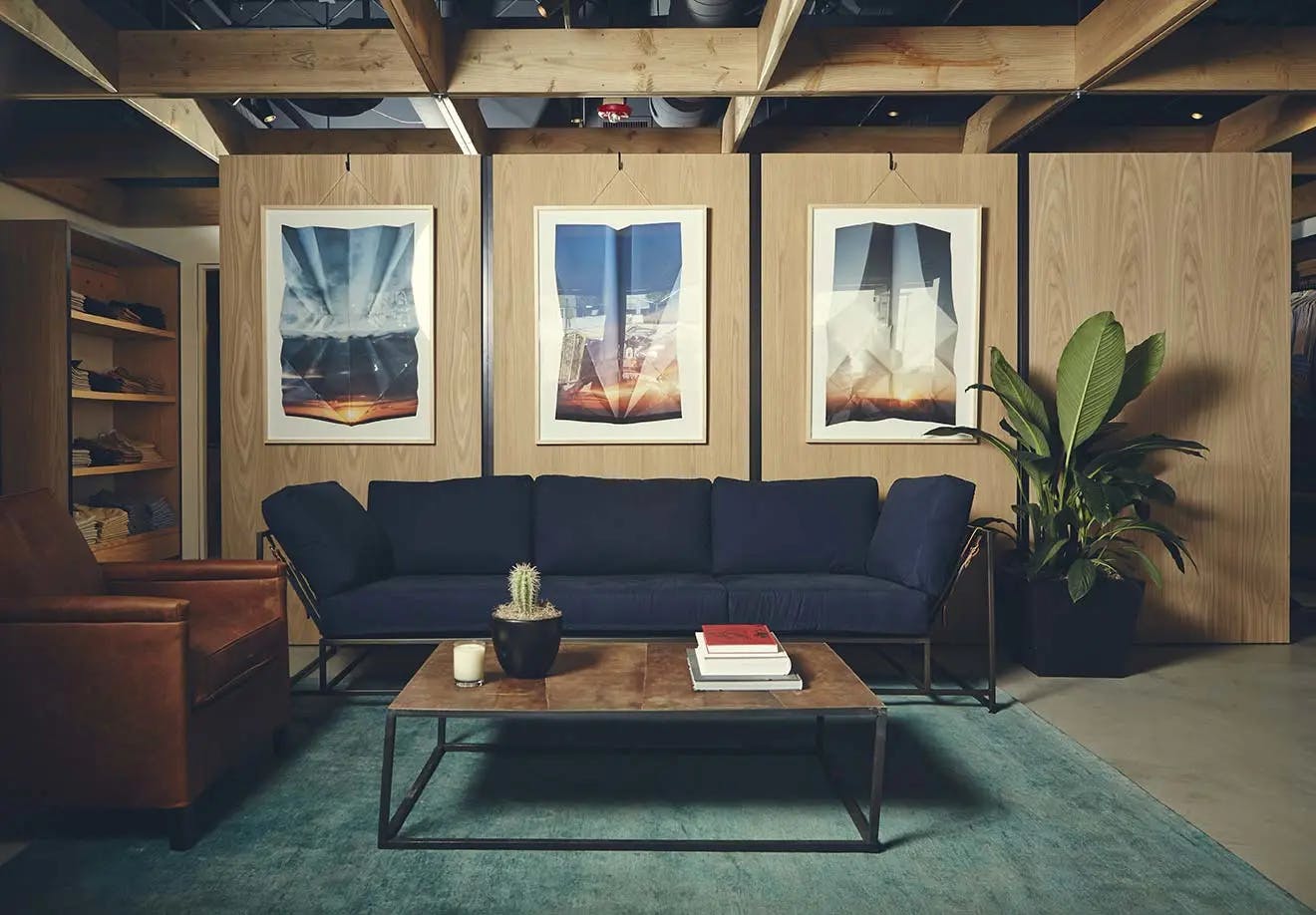 Three framed photographs of cloudy skies by artist Millee Tibbs on a wood wall above a blue sofa at a Bonobos store in Los Angeles.