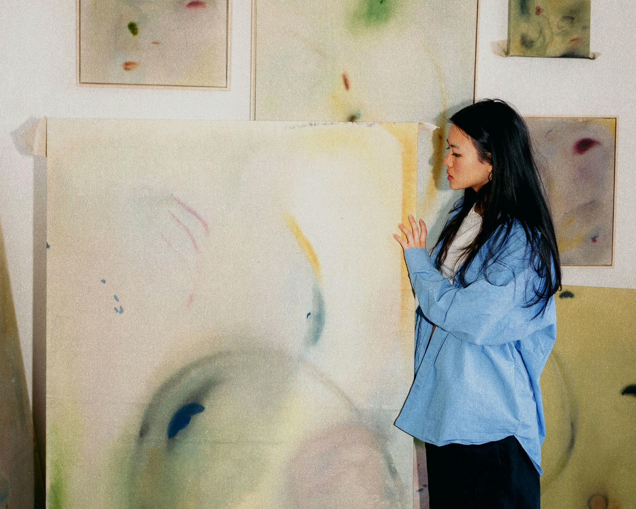 Artist Arlina Cai holding a large, abstract painting in her studio.