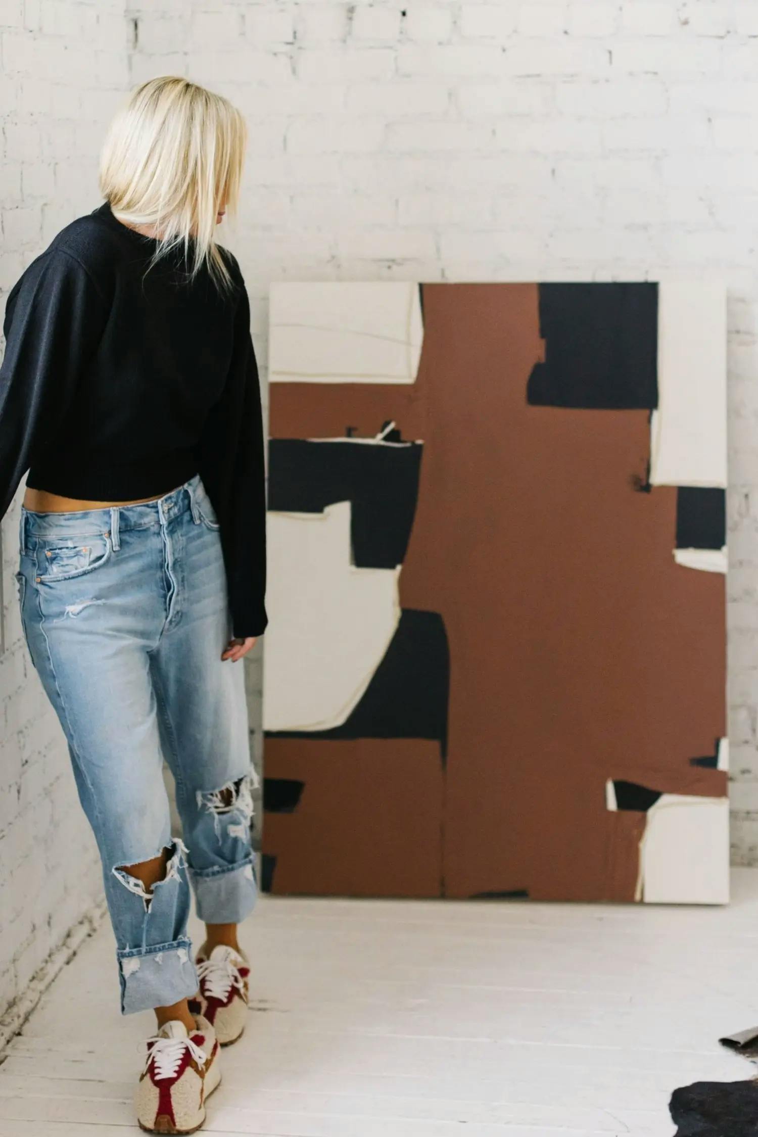 Artist Holly Addi standing next to a patchwork, terracotta and black painting in her studio.
