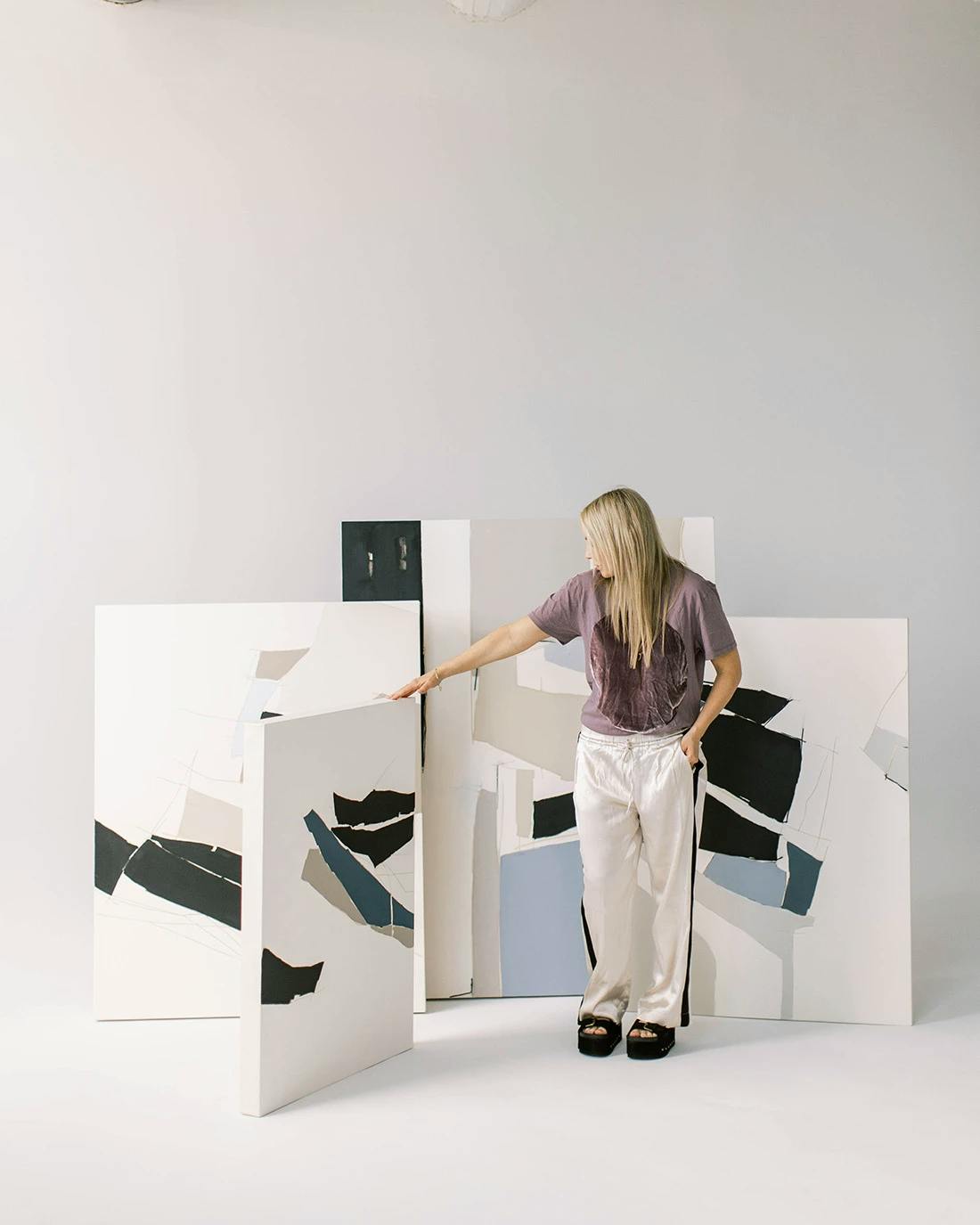 Artist Holly Addi in her studio surrounded by her neutral and blue paintings on canvas.