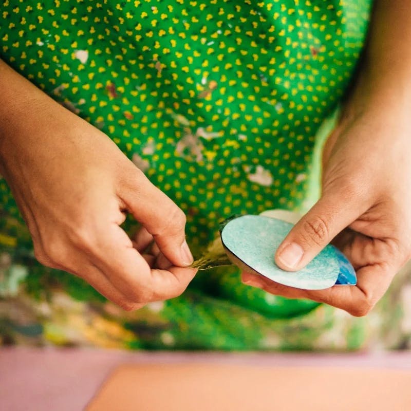 Artist Xochi Solis wearing a bright green dress, holding circular pieces of colored paper in her studio.
