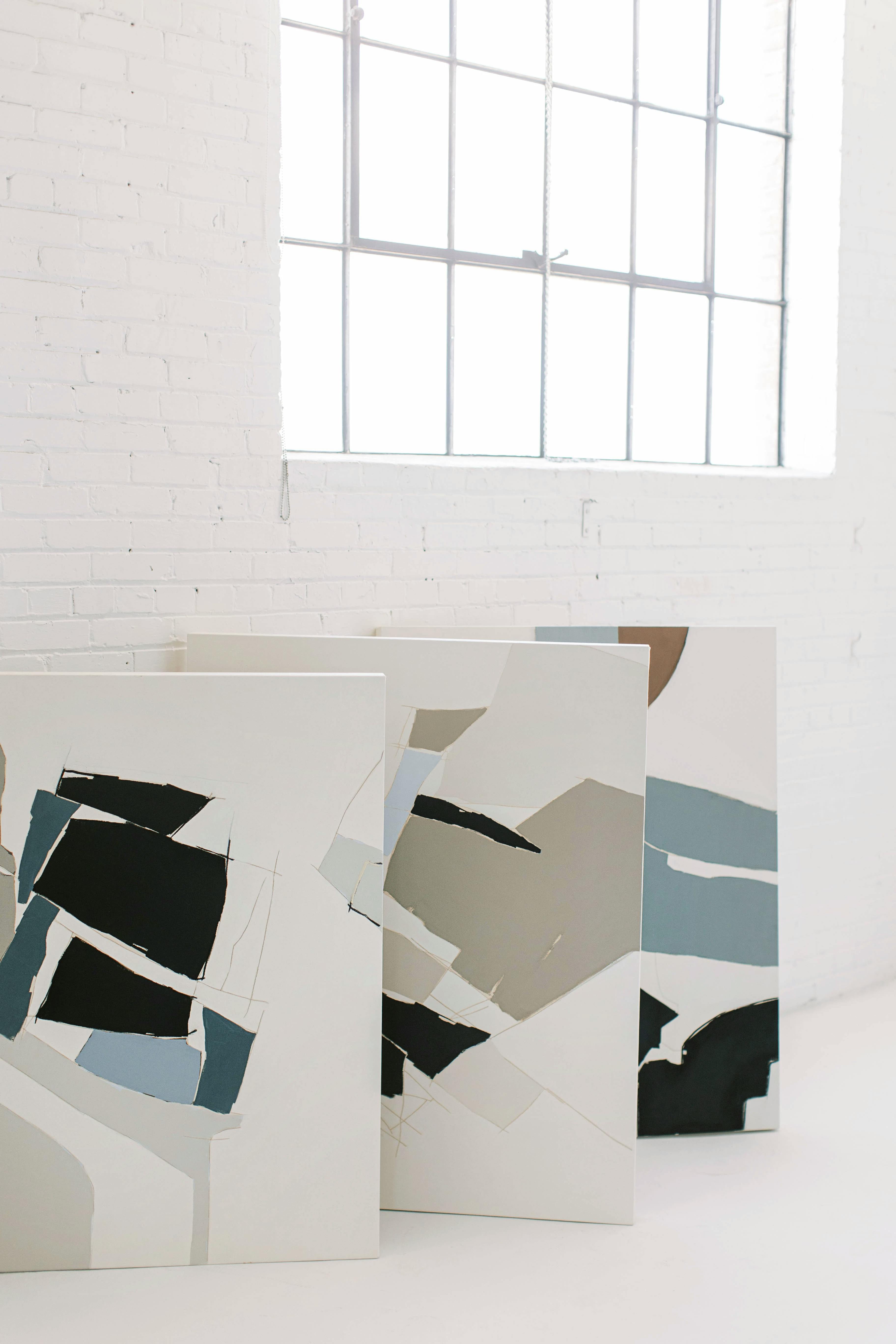 Three abstract, geometric paintings by artist Holly Addi in her white brick studio.