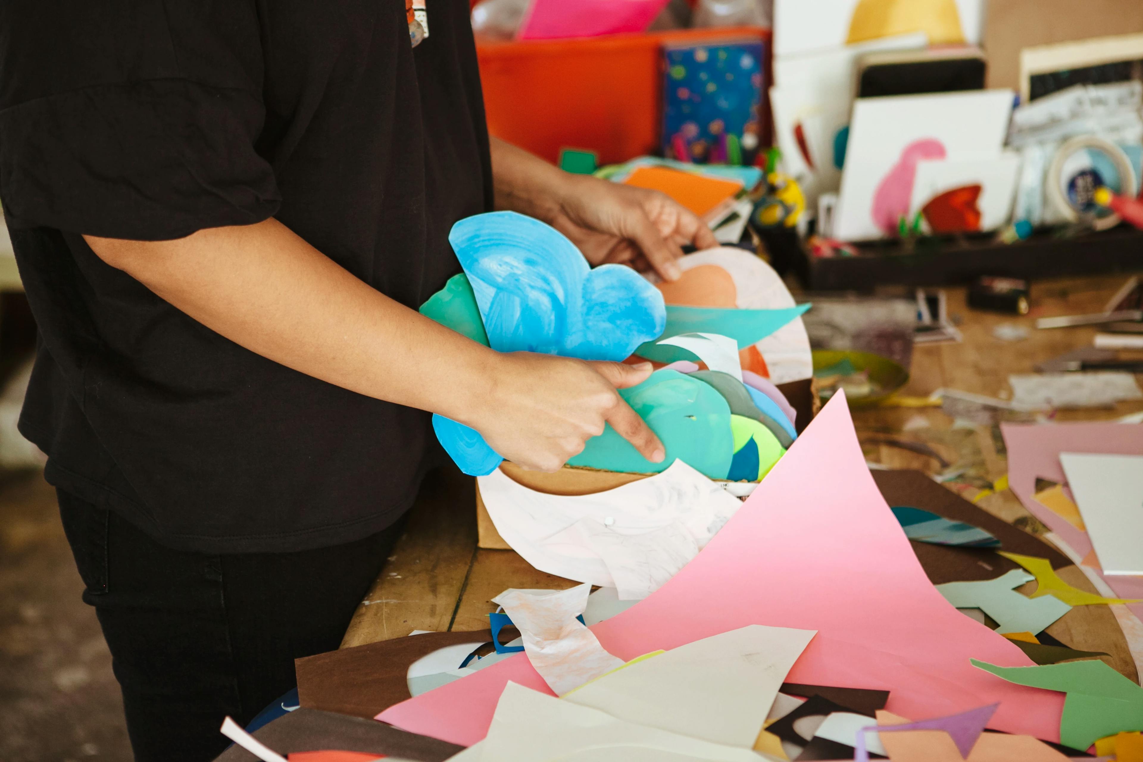 Artist Xochi Solis holding pieces of cut-up colored paper for her collages.