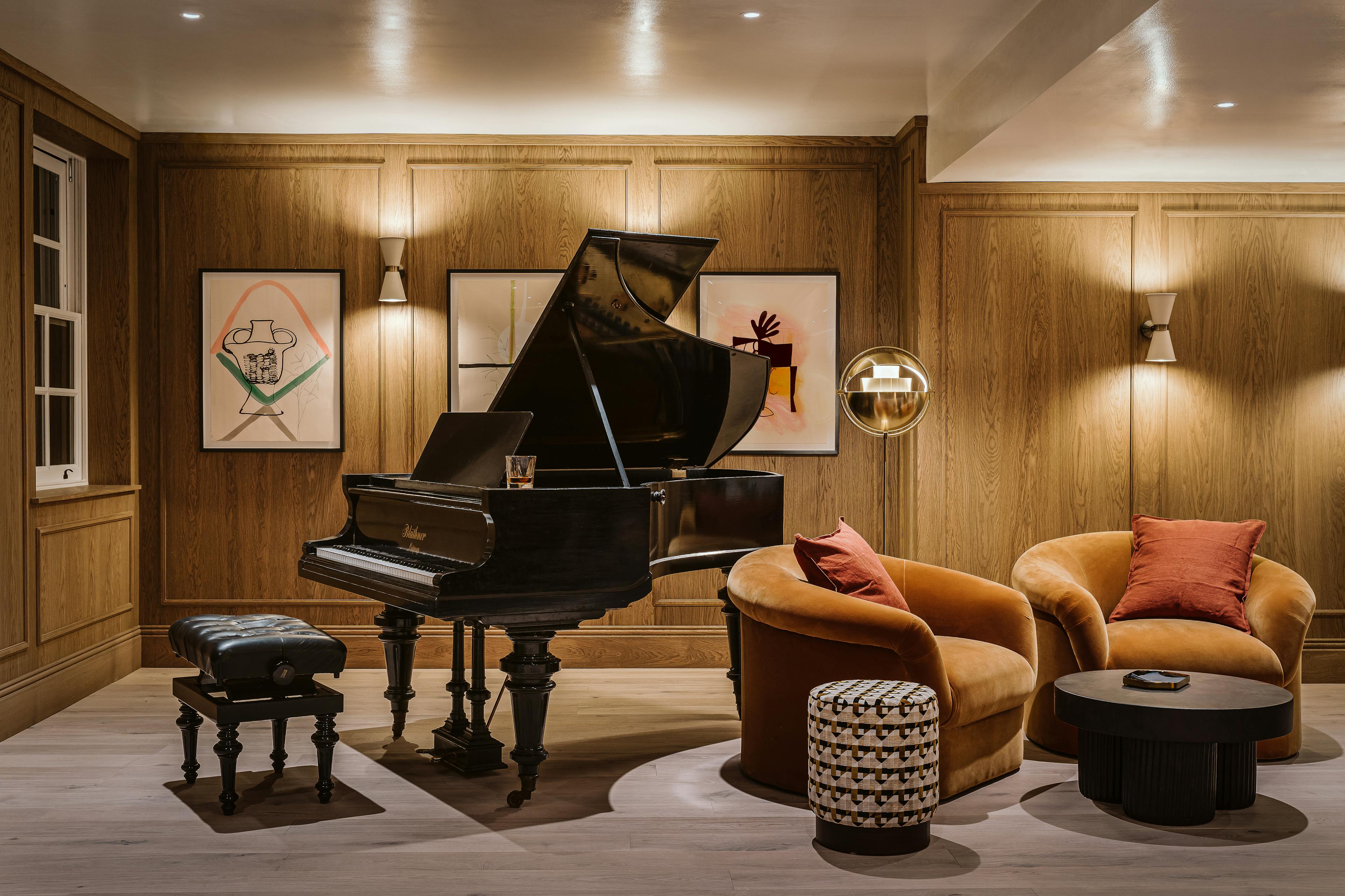 A row of three framed abstract drawings by artist Vicki Sher installed on wood panel wall behind a baby grand piano at the Chief London clubhouse.