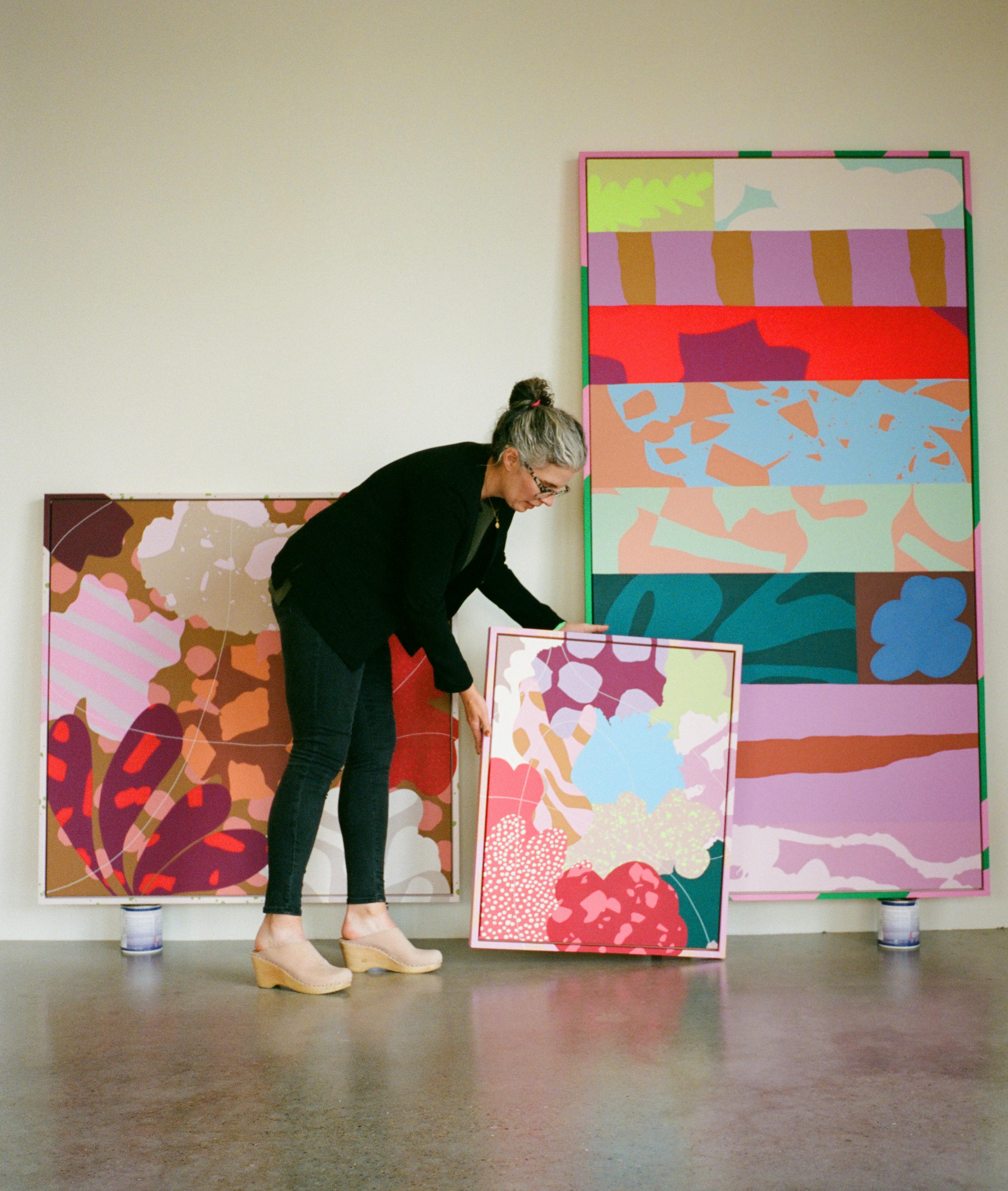 Artist Alex Proba standing next to three of her colorful abstract paintings.