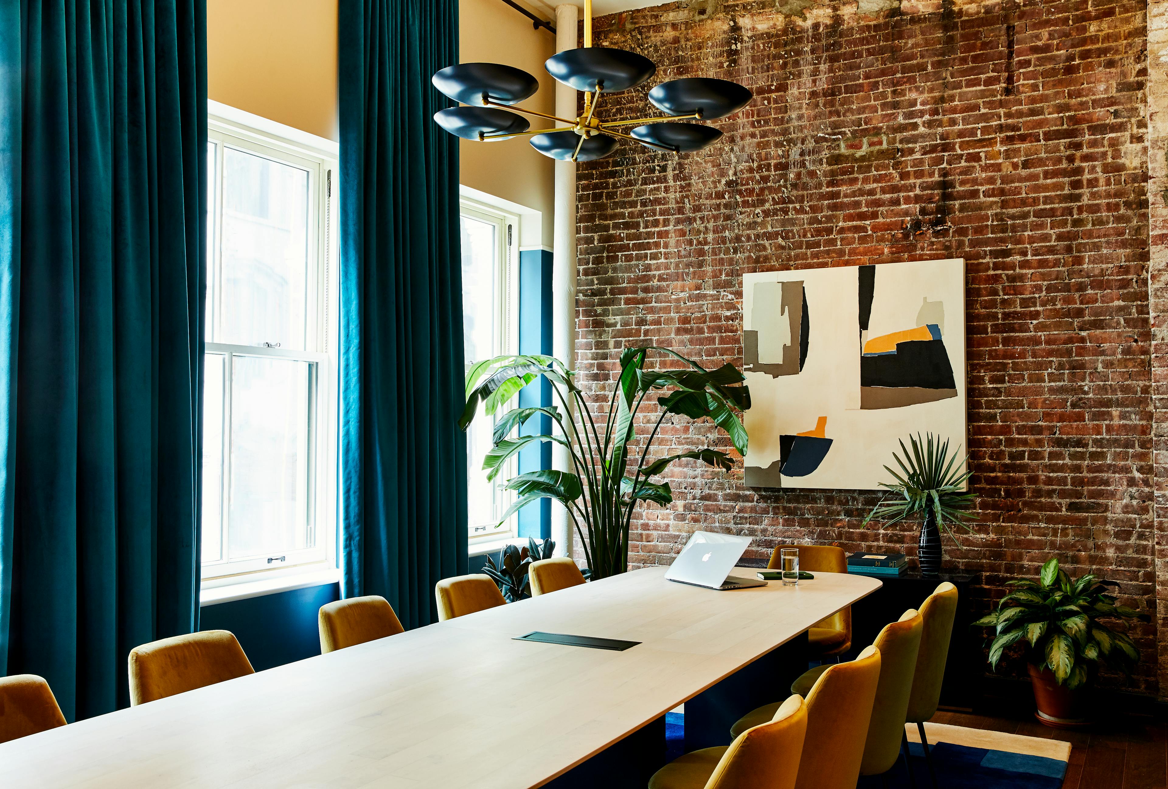 A boardroom at the Chief Flatiron Clubhouse, featuring a long wooden table and an abstract painting by artist Holly Addi installed on a brick wall.
