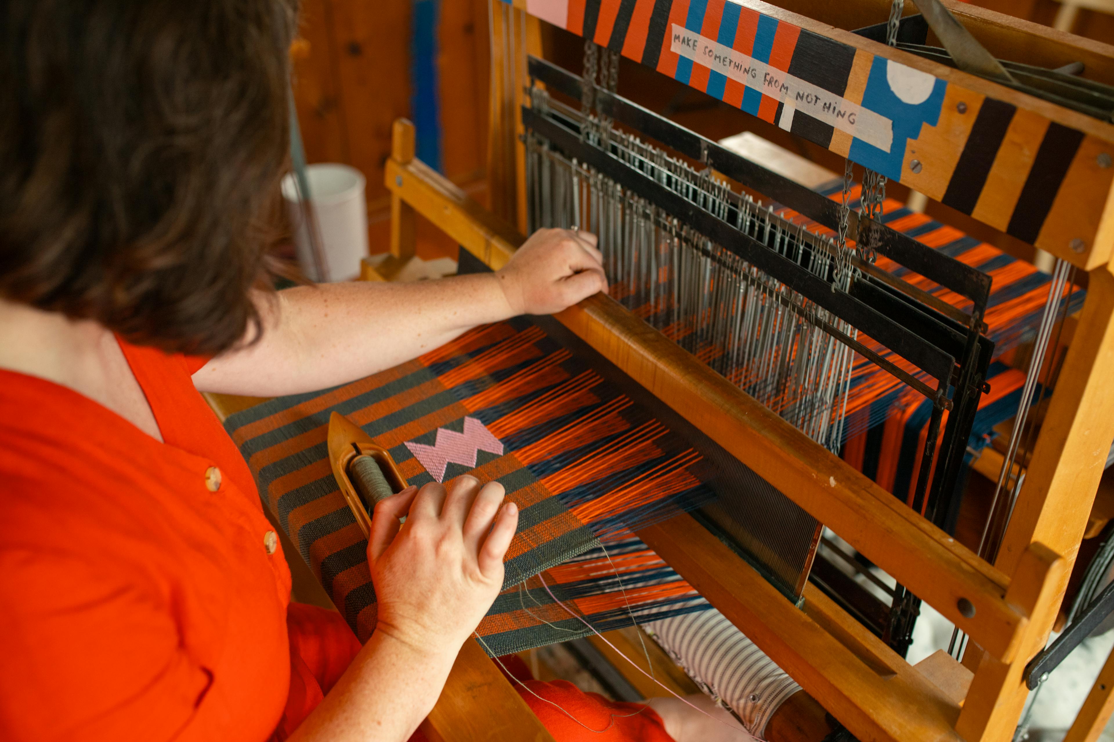 Close-up of artist Sarah Sullivan Sherrod using a loom to create striped, handwoven textiles.