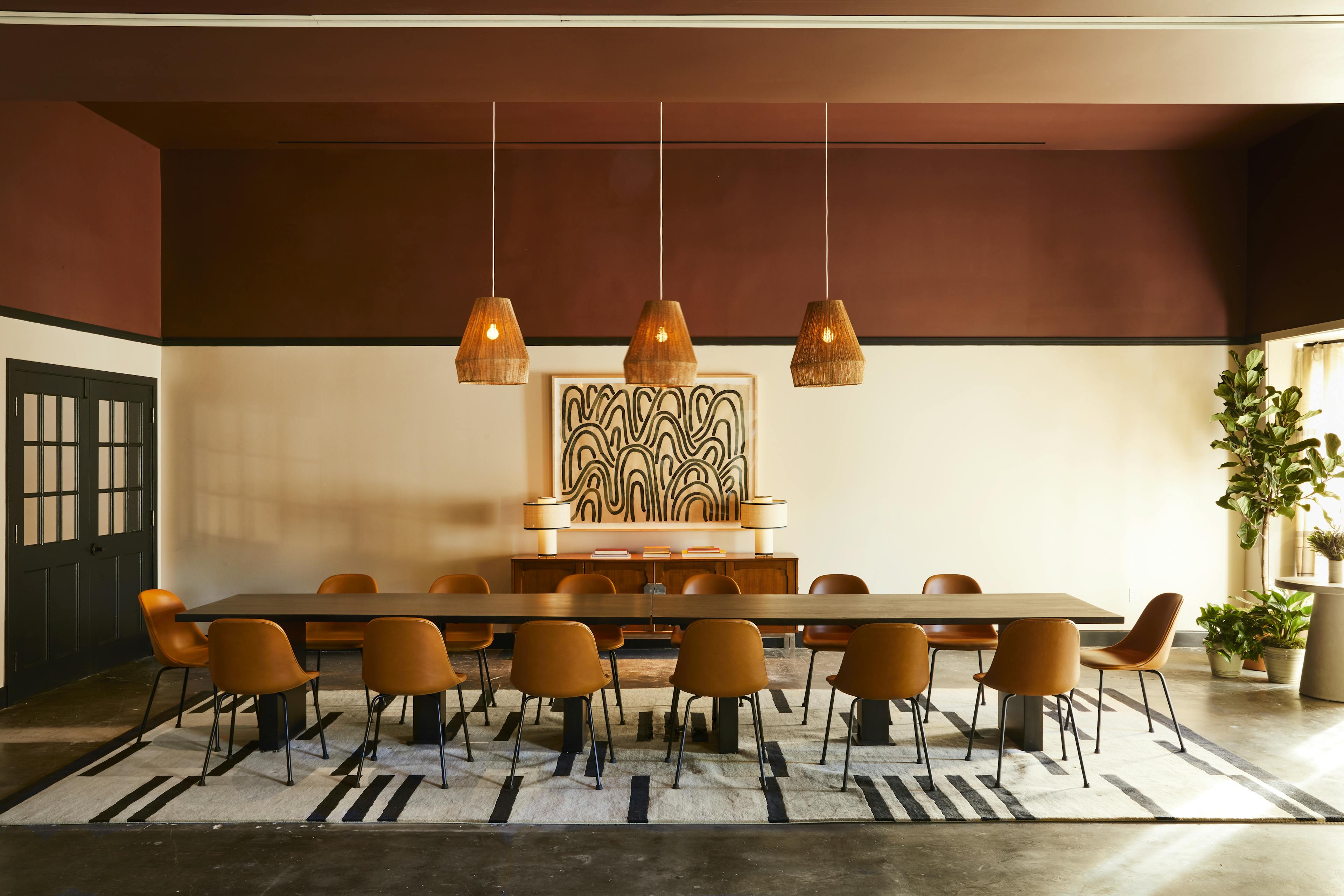 An orange boardroom at the Chief Los Angeles Clubhouse, with a long rectangular table and chairs and an abstract, linear artwork by artist Kate Roebuck installed on a wall.