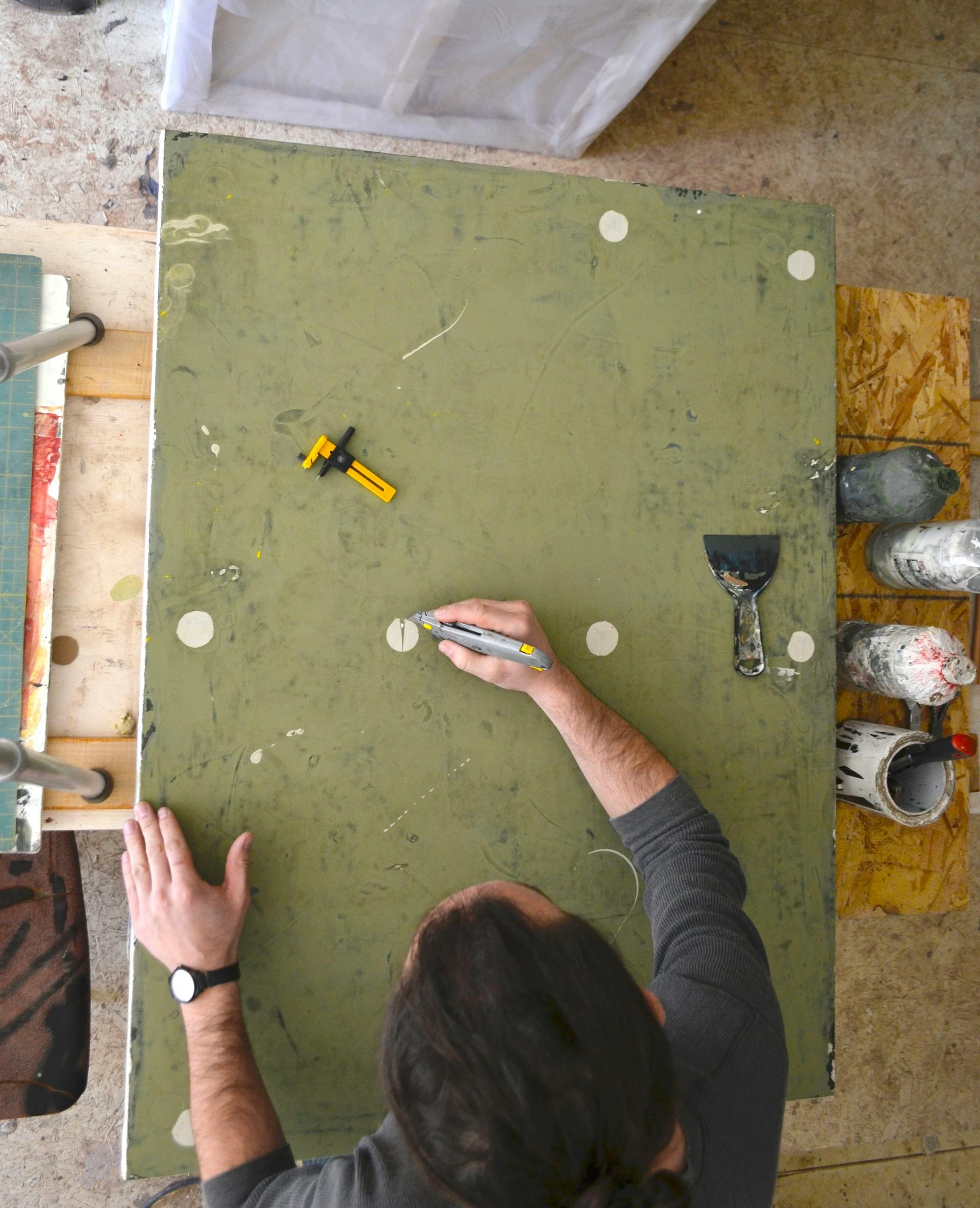 Aerial view of artist Clay Mahn working on a distressed green canvas in his studio.
