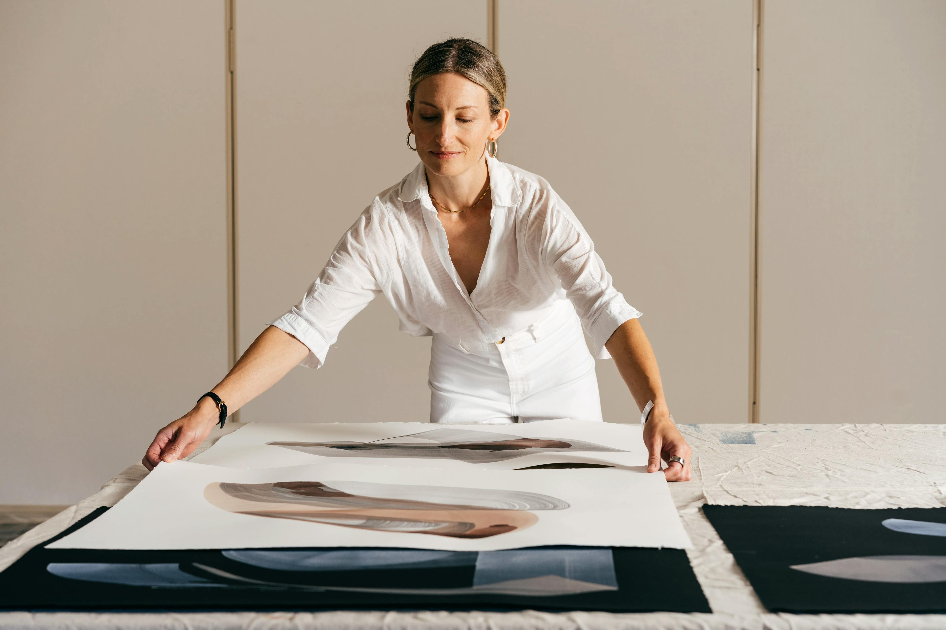 Artist Laura Naples moves large paintings on paper across a table at MacArthur Place.