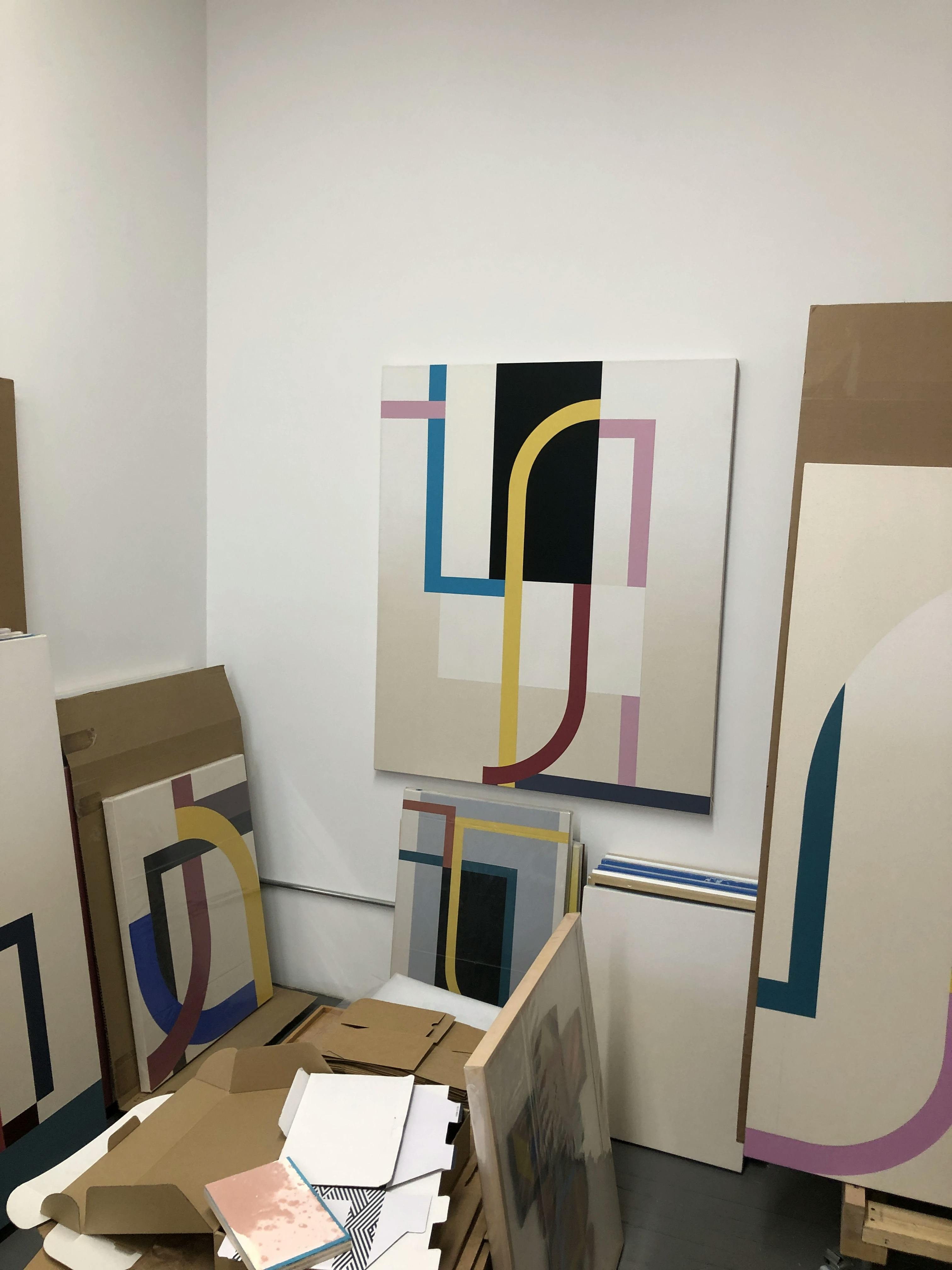 Multiple abstract, geometric paintings by artist Christian Nguyen installed and propped up against the wall in his studo.