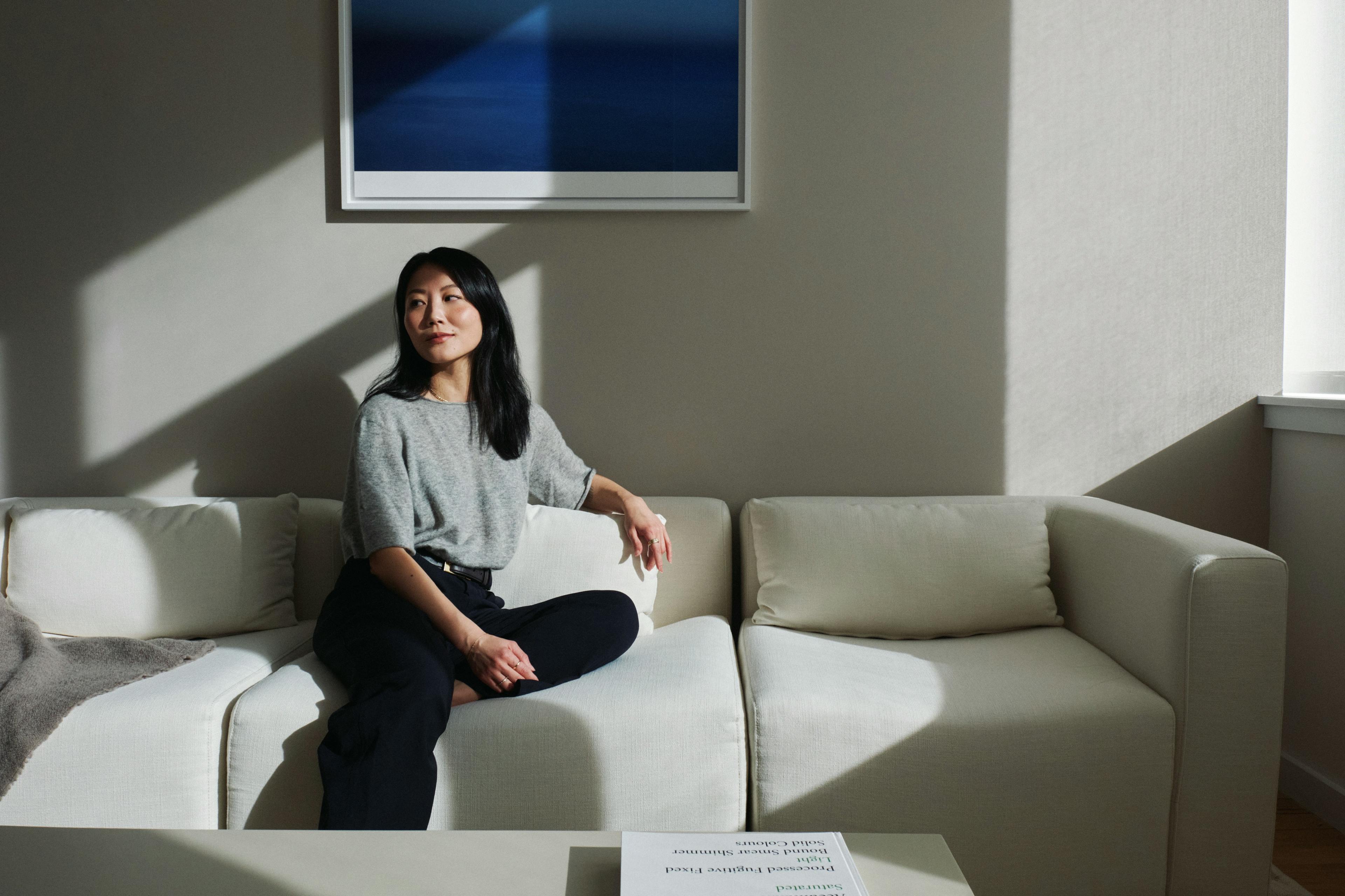 Alice Gao sitting on a white couch in her home below a blue, framed artwork.