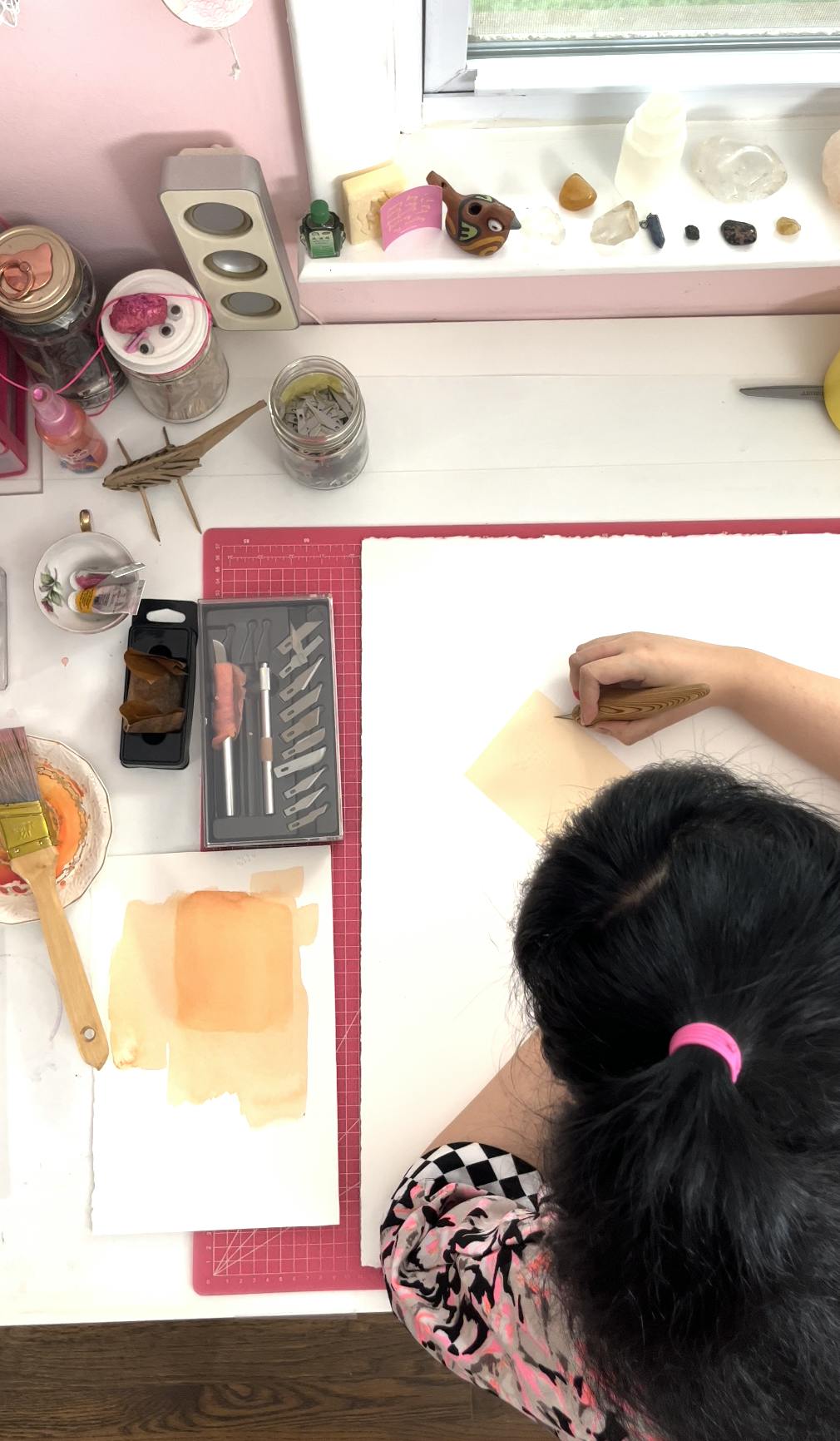 An aerial view of artist Lucha Rodríguez working in her studio on a pink mat.