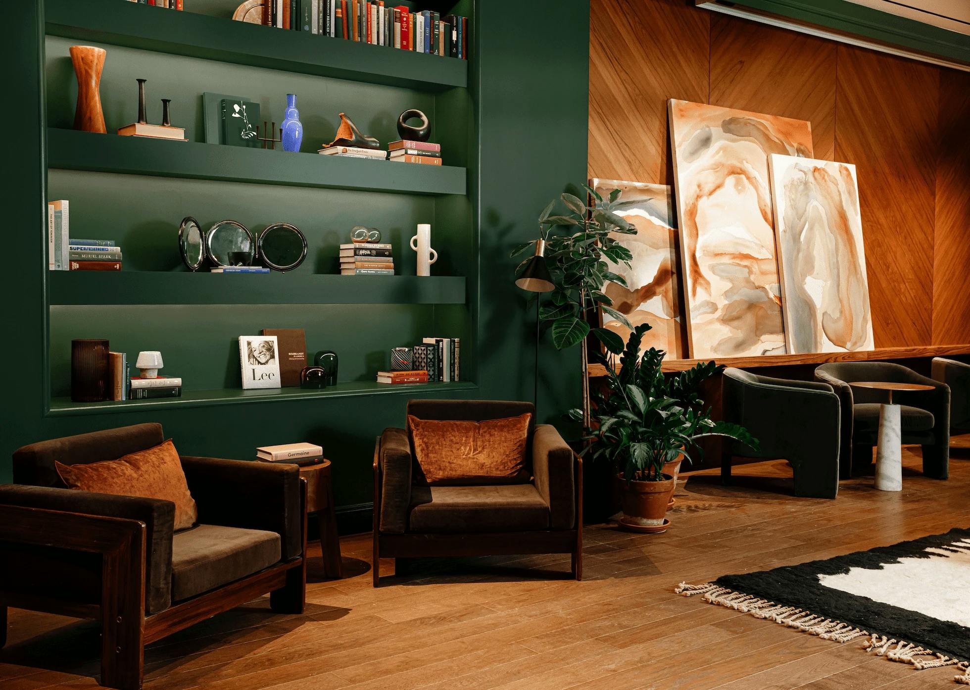A dark green bookcase in the Chief Flatiron Clubhouse next to three abstract paintings by Erin Lynn Welsh.
