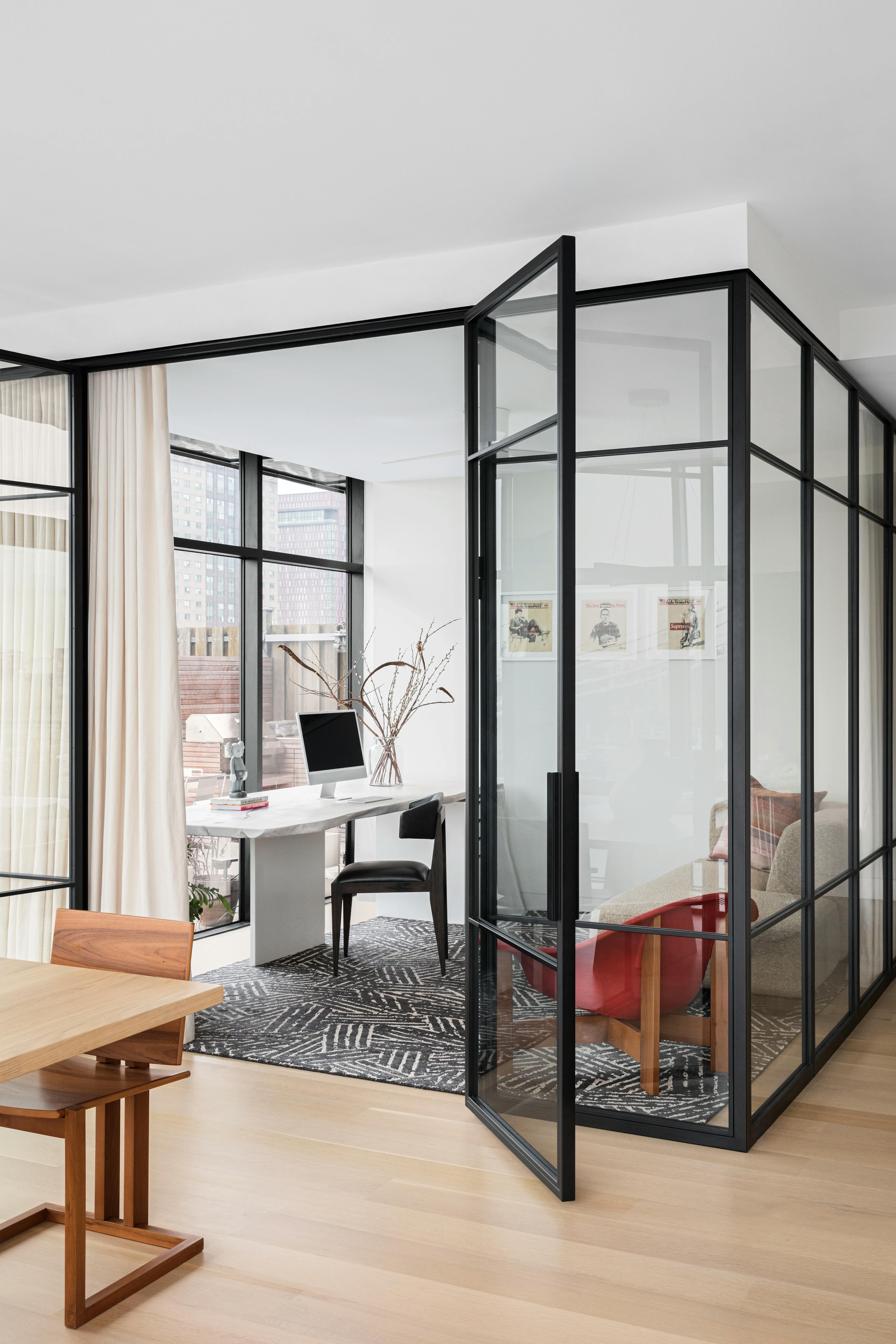 Glass-enclosed home office with a white desk and red chair within a Brooklyn apartment.