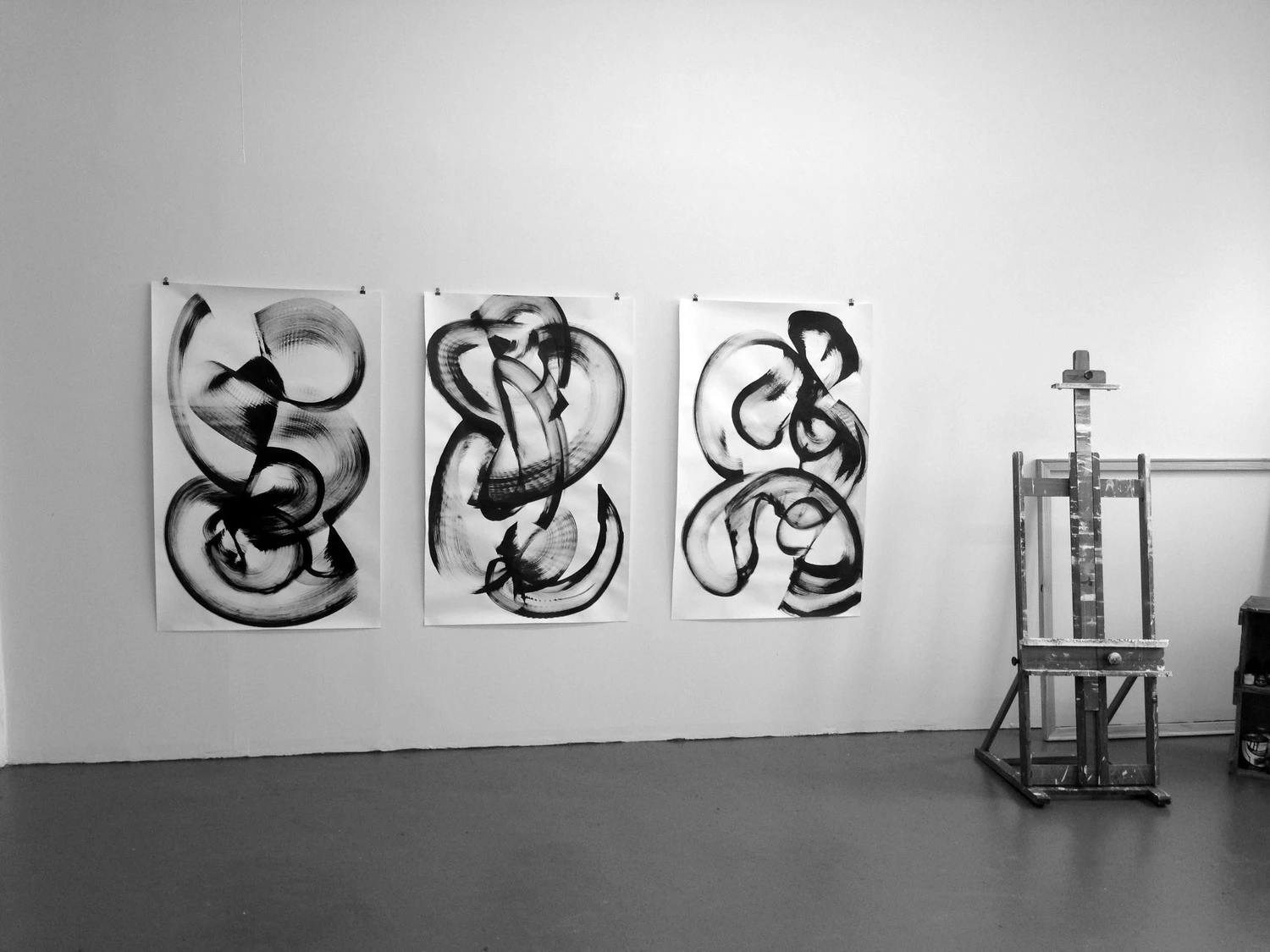 Three works of paper with circular swaths of ink by artist Thomas Hammer on a white wall in his studio next to a metal easel.