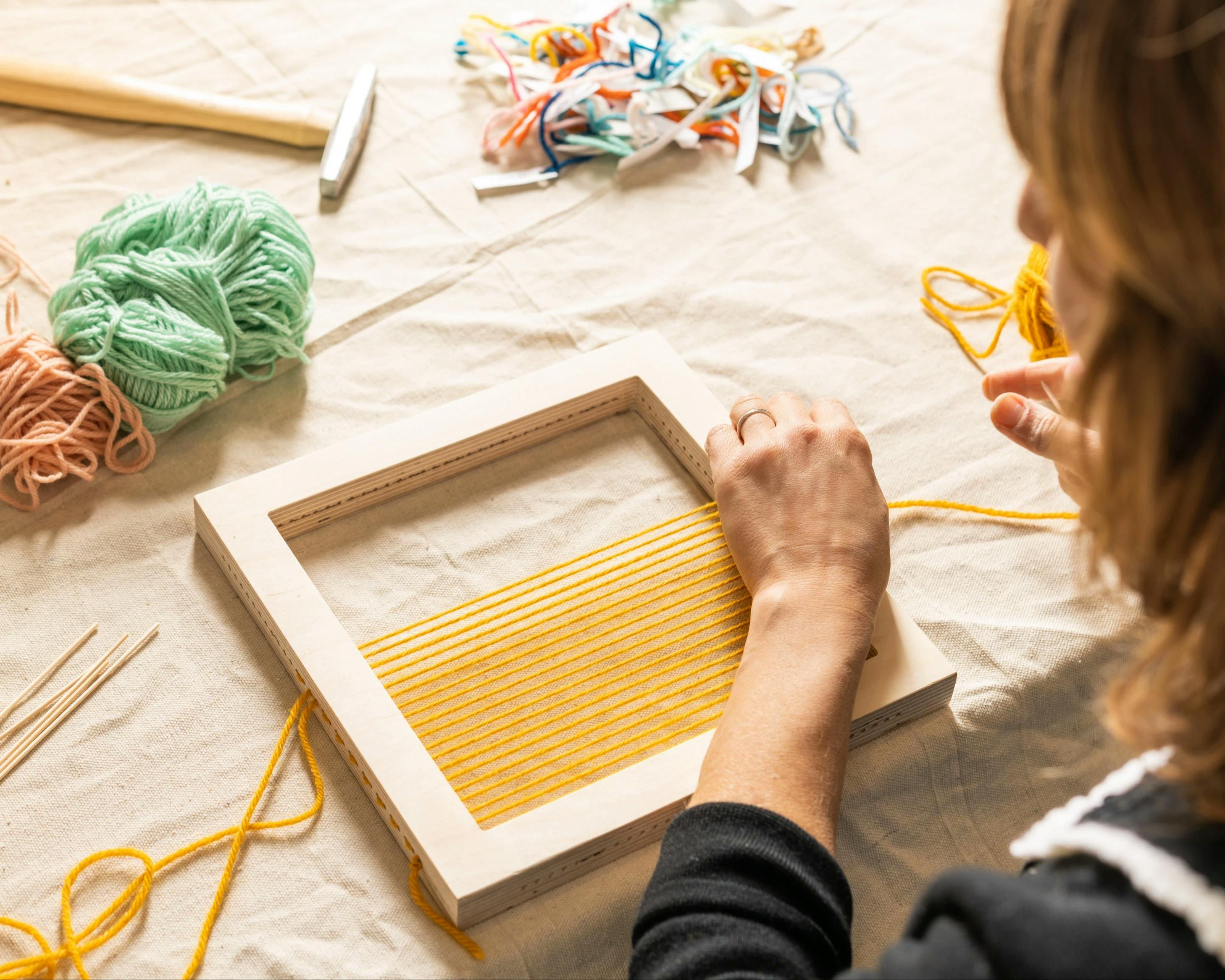 Artist Hayley Sheldon pulling yellow thread through a wood frame at MacArthur Place.