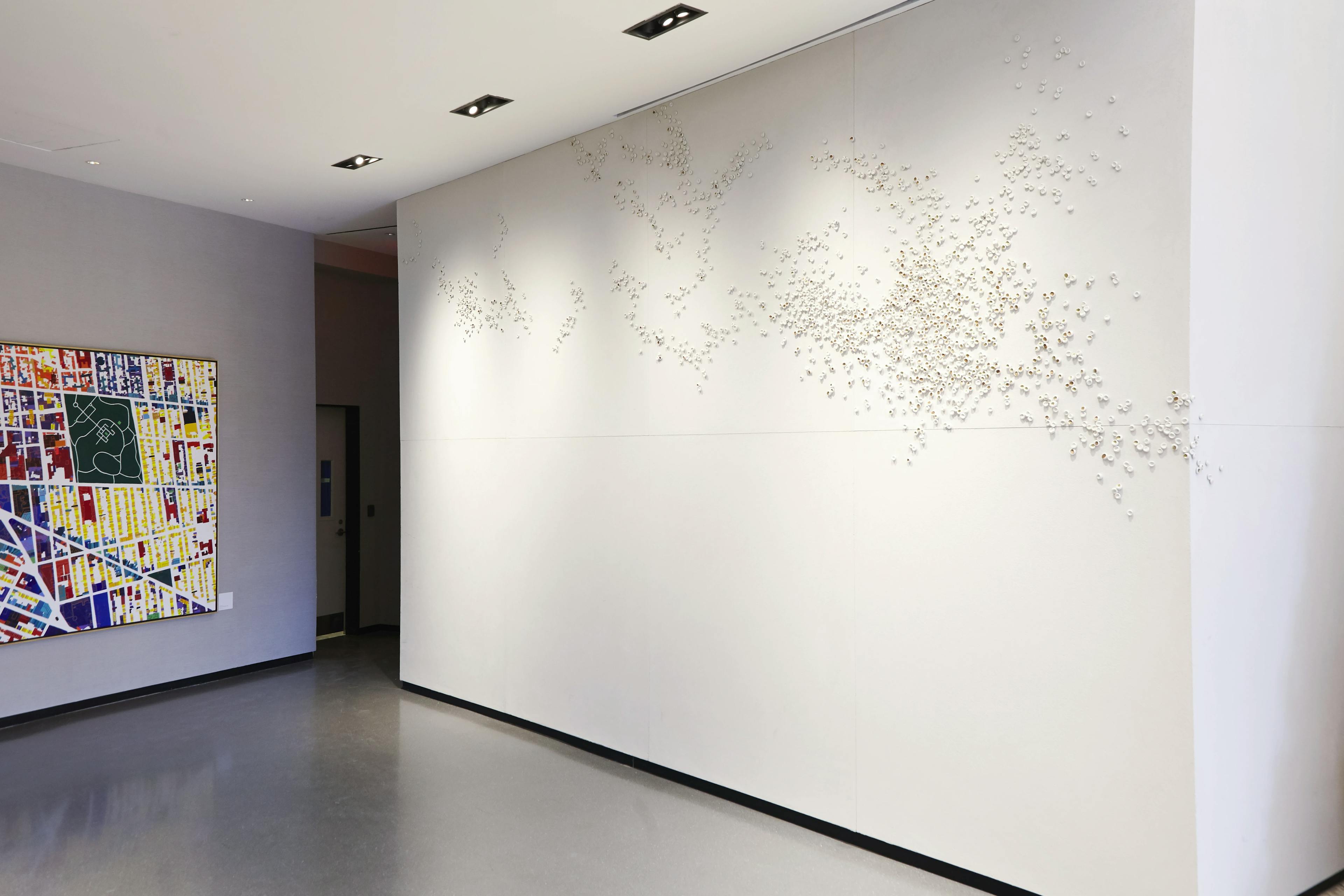 Site-specific installation of tiny porcelain pieces by artist Christina Watka arranged in an organic pattern on a white wall.