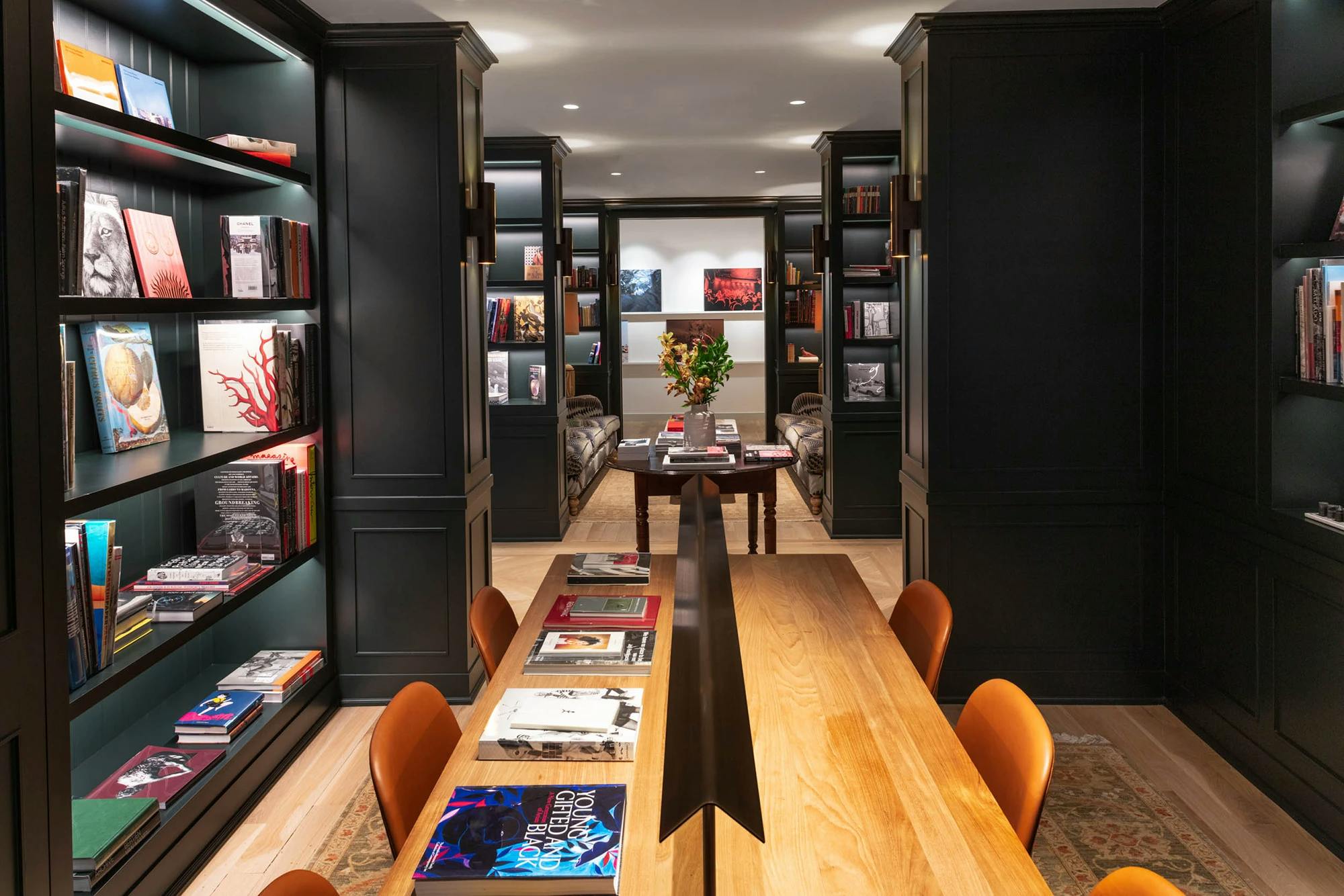 The library area at FIG with a wood table and dark green shelves filled with colorful books.