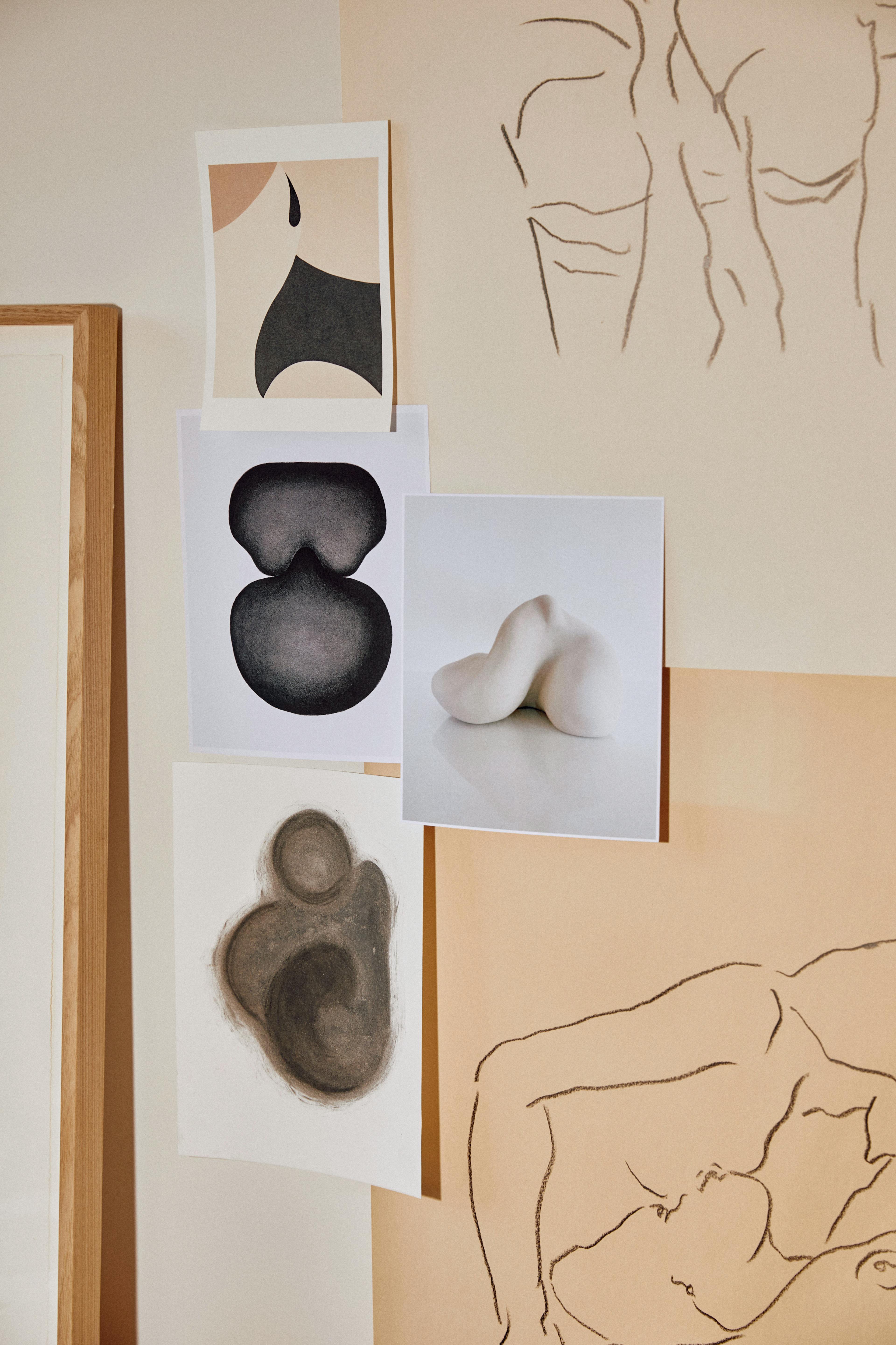 Six images of black, white, and tan figures pinned to a wall in Caroline Walls' studio.