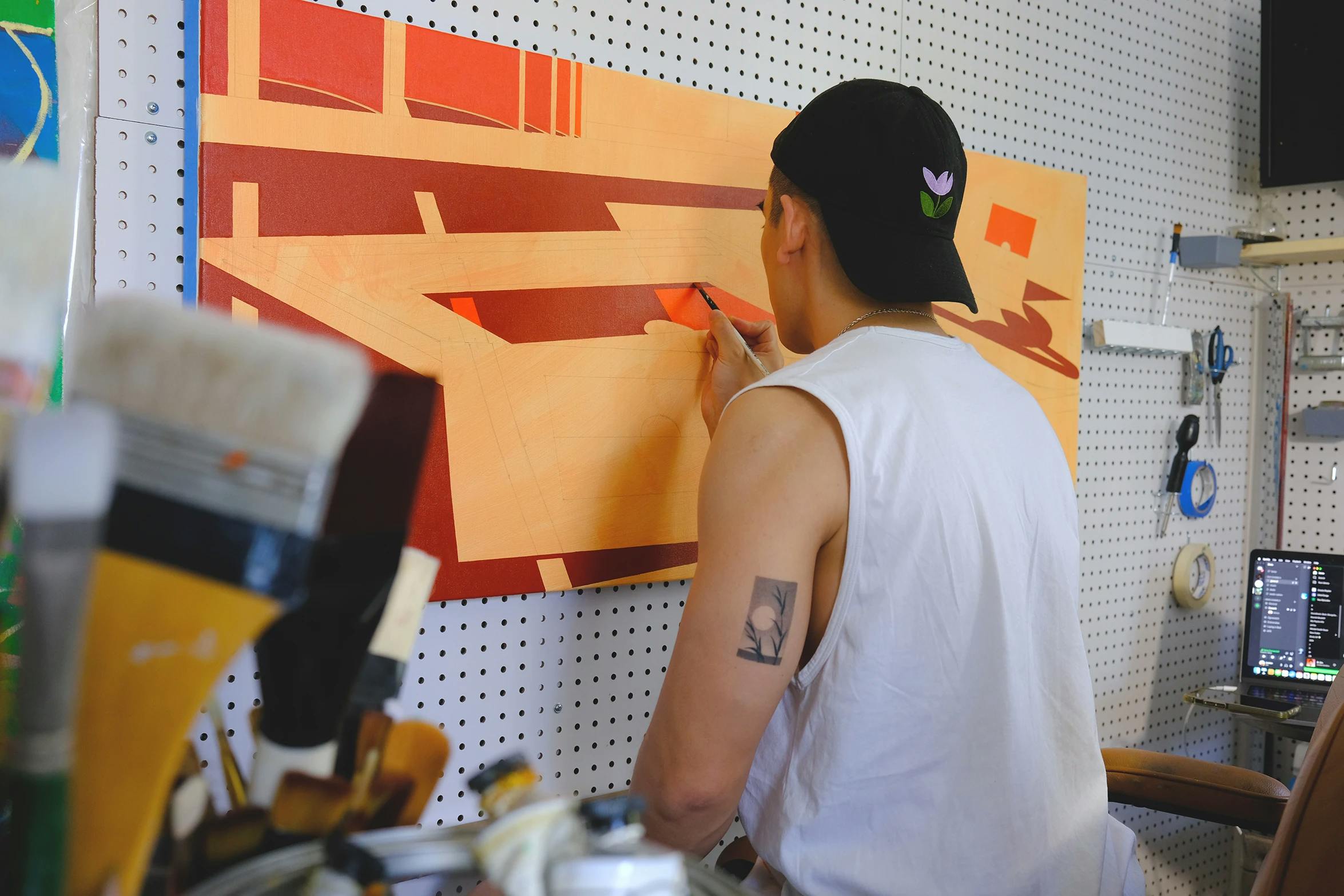 Artist Adrian Kay Wong painting an abstract, geometric orange canvas in his studio.
