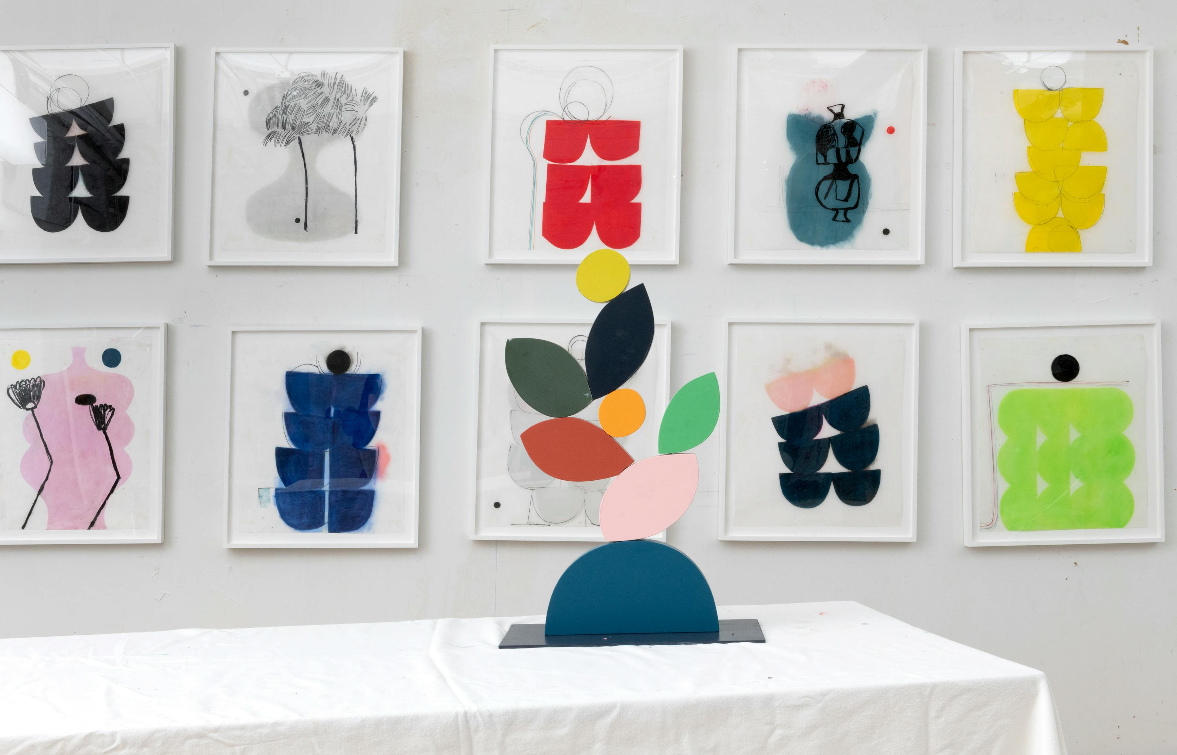 Framed paintings and a colorful, tabletop sculpture by artist Vicki Sher in her studio.