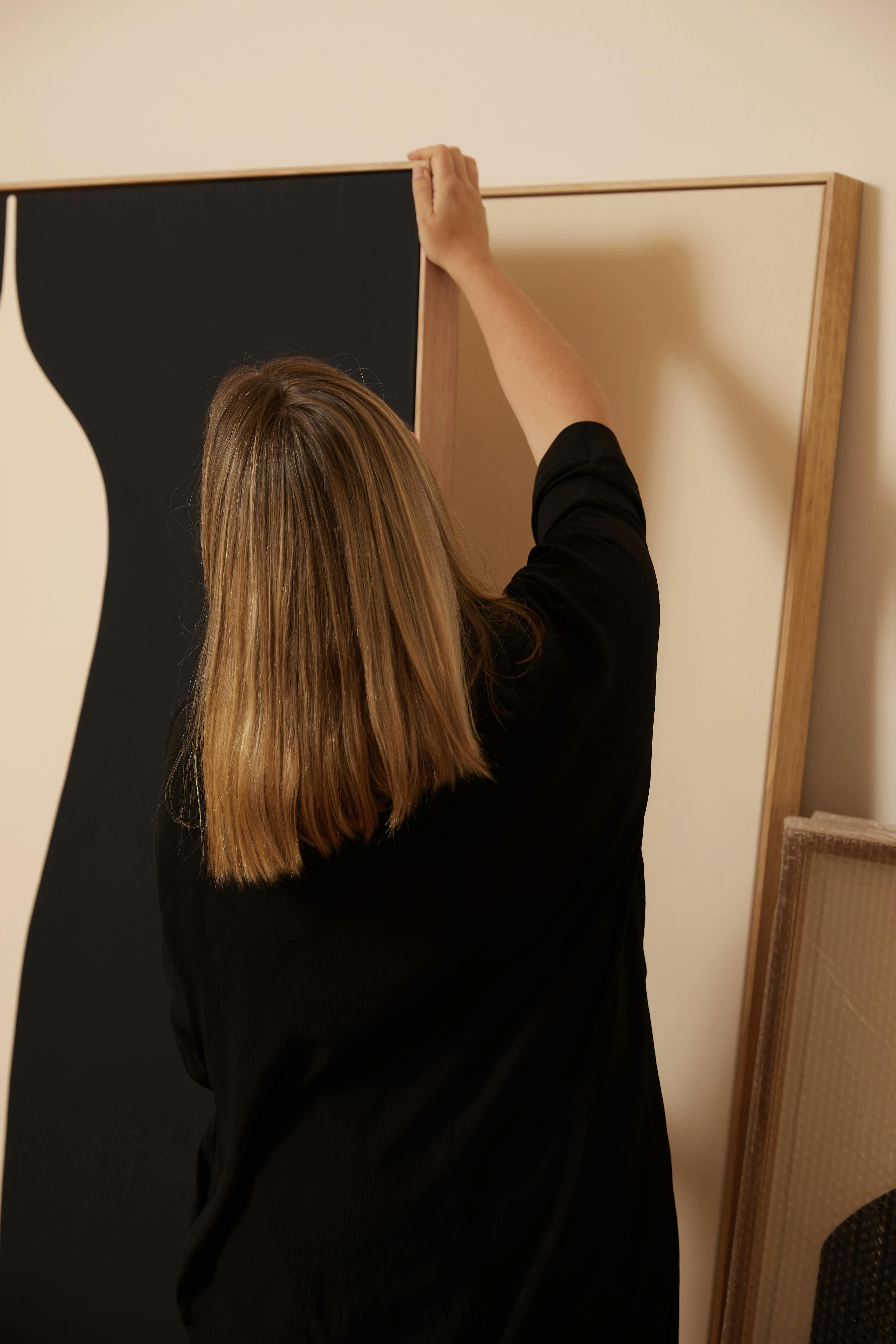 The back of Caroline Walls as she flips through black and white paintings in her studio.