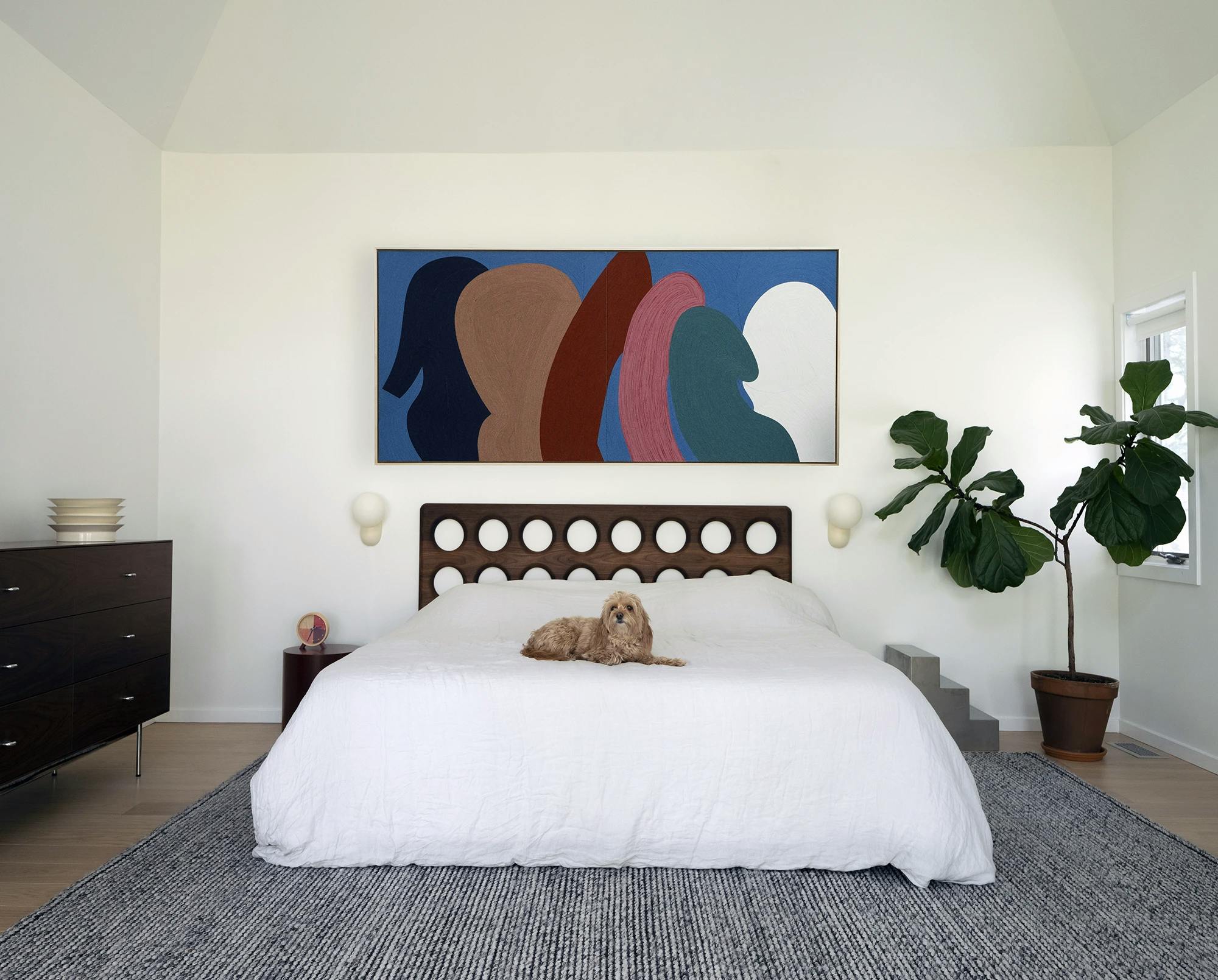 Artwork by Paola Rodriguez Arias above a bed with a wooden headboard. 