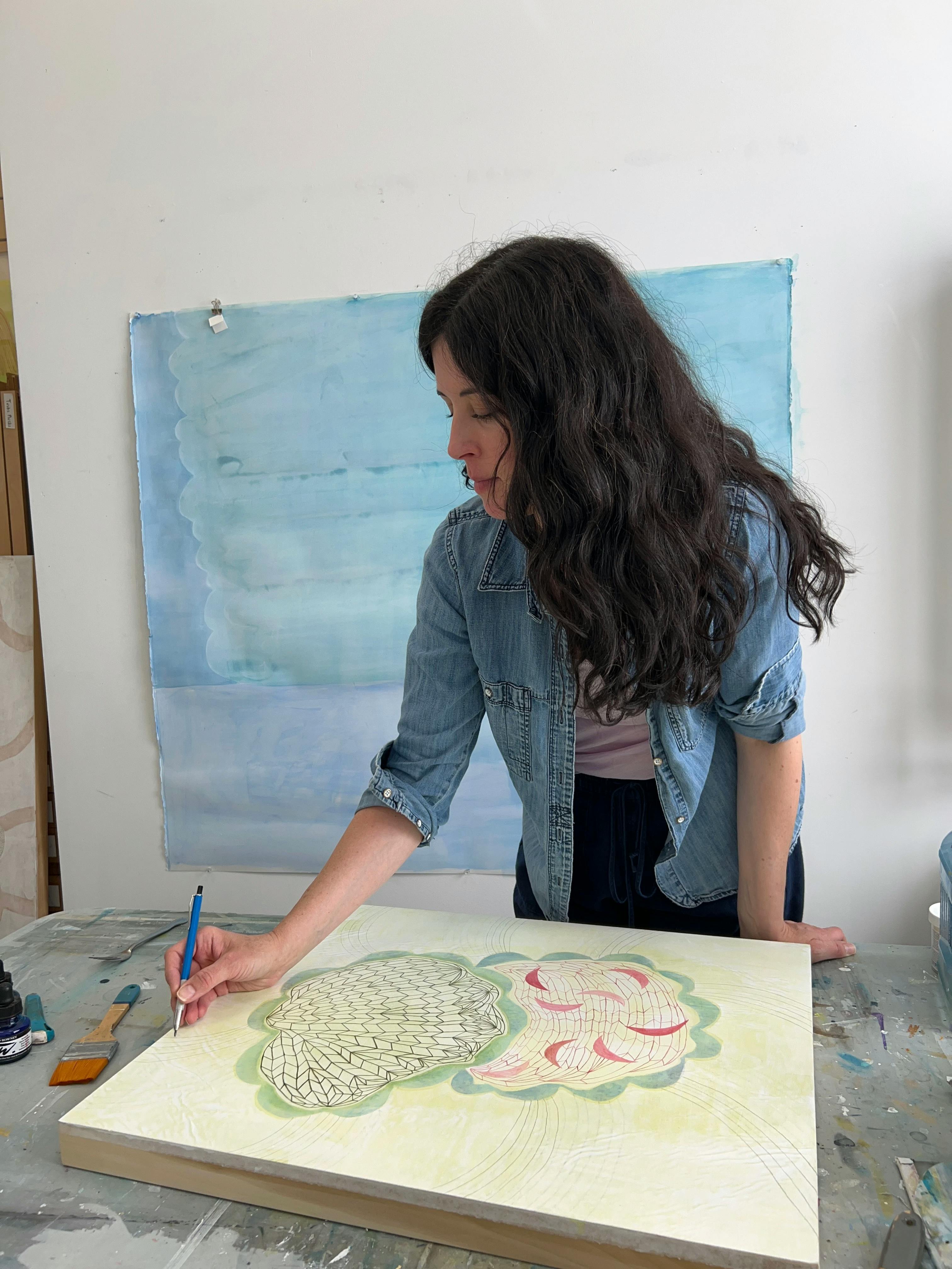 Artist Lydia Bassis standing and using a pencil on a yellow canvas in her studio.