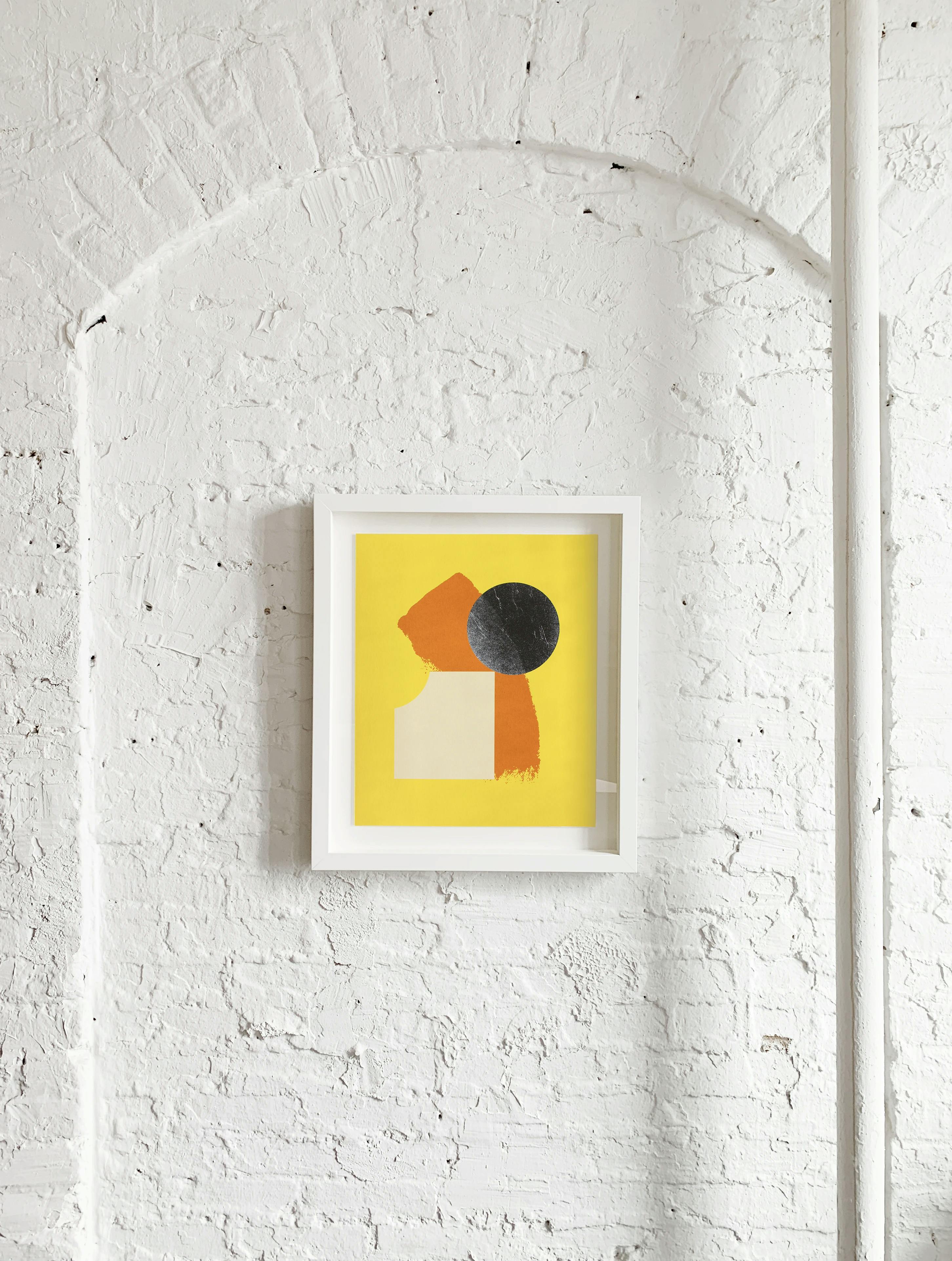 Chad Kouri's print Opportunity for Reflection (Yellow) framed on a white brick wall.