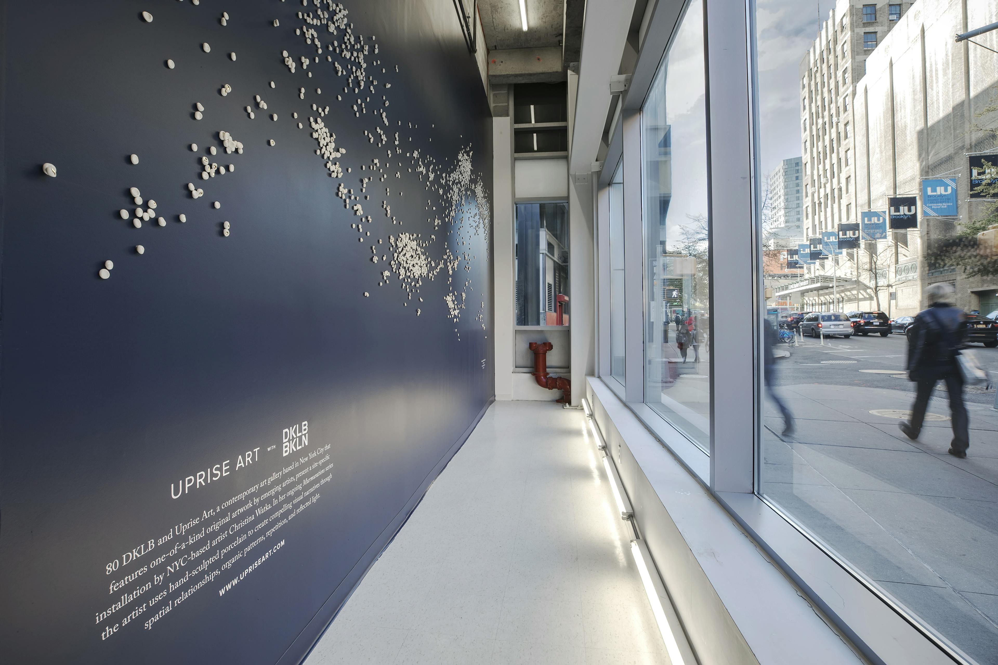 Custom porcelain installation by artist Christina Watka on a dark blue wall facing floor-to-ceiling windows that overlook onto a busy New York street.