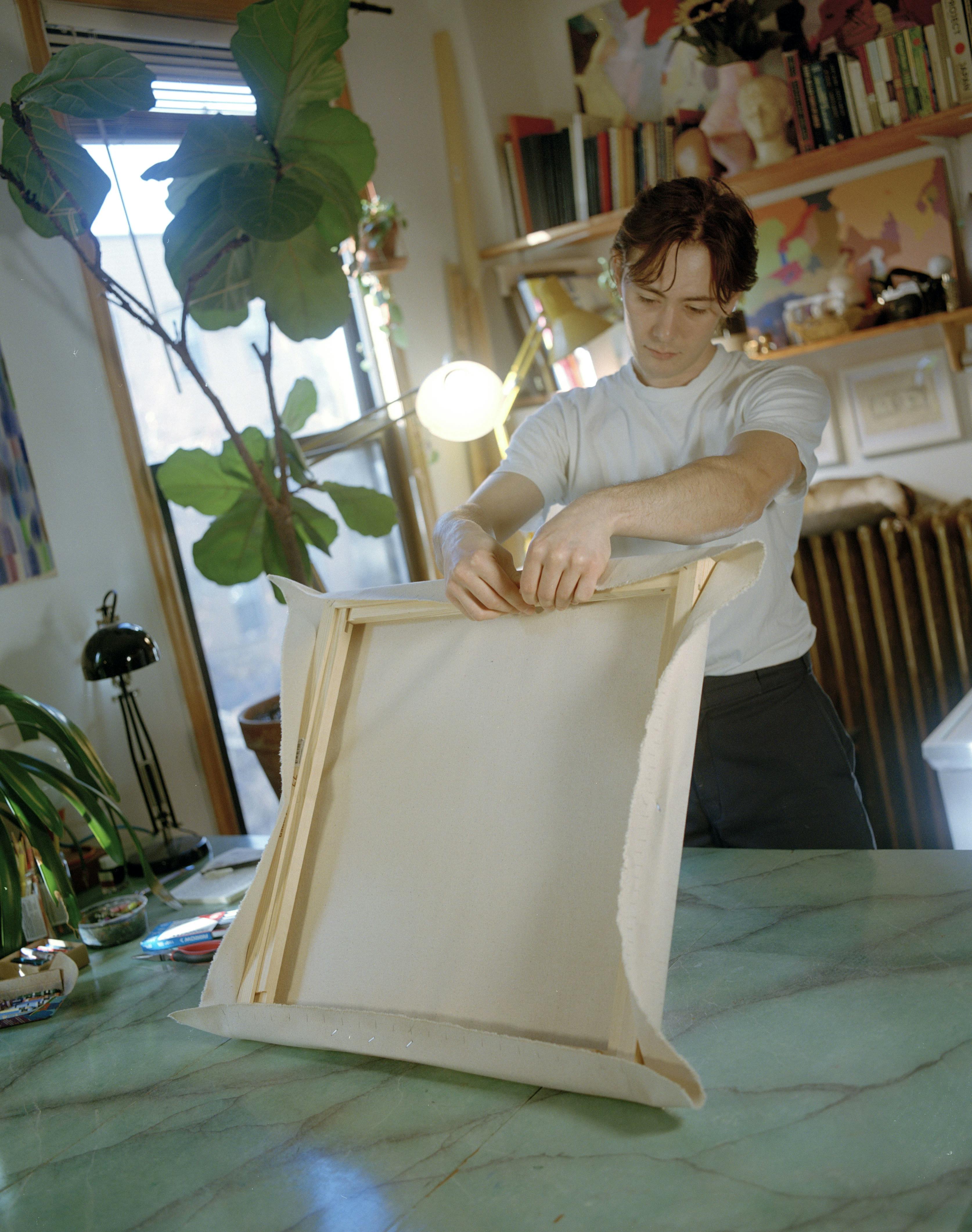 Artist Devon Reina stretching his canvas onto a wooden frame.