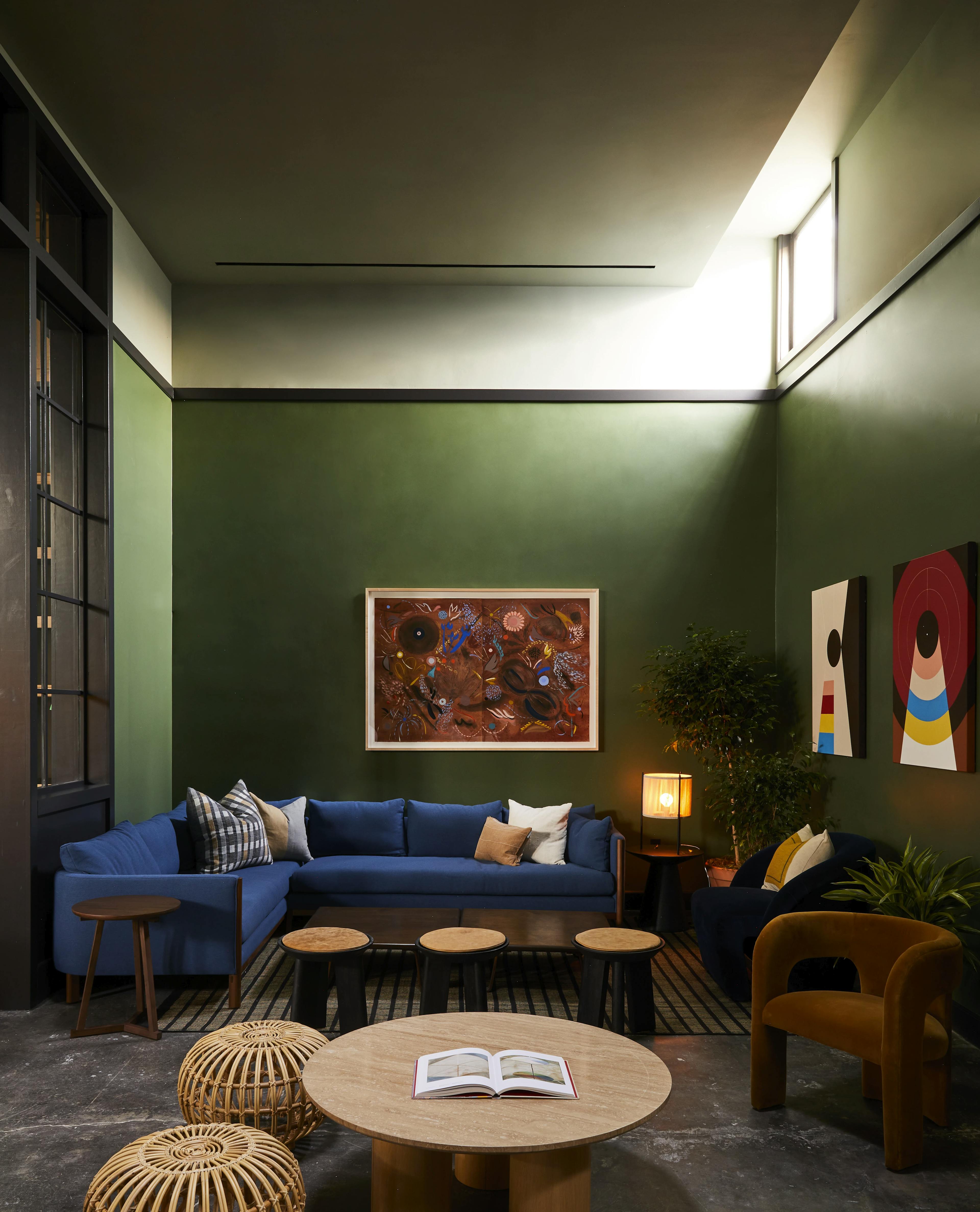 A green lounge area at the Chief Los Angeles Clubhouse, featuring one framed floral artwork by artist Kayla Plosz Antiel and two abstract, geometric paintings by artist Kimmy Quillin installed on the wall.