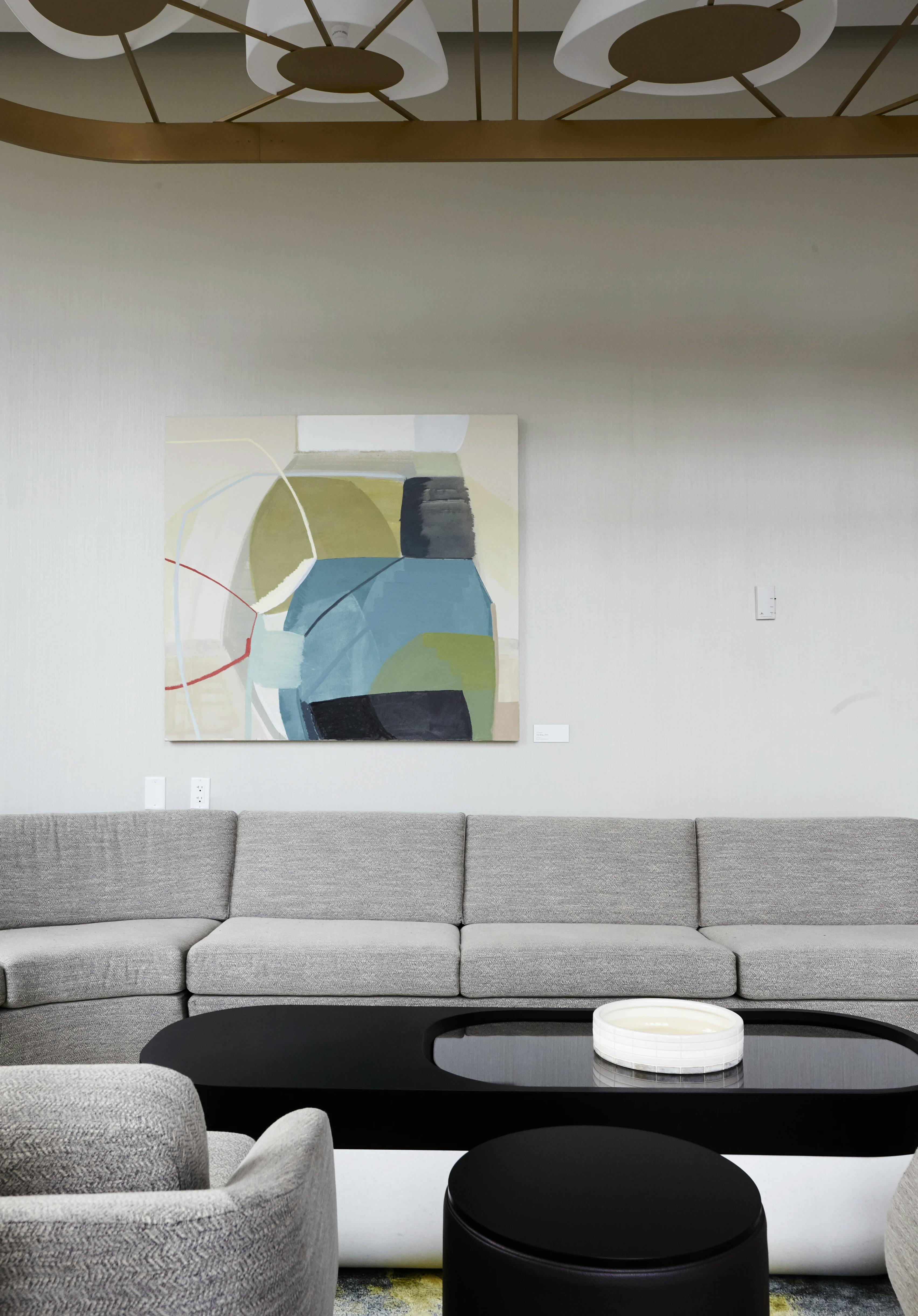 Gestural abstract painting on canvas by artist Ky Anderson installed above a grey sectional sofa in a lounge area.