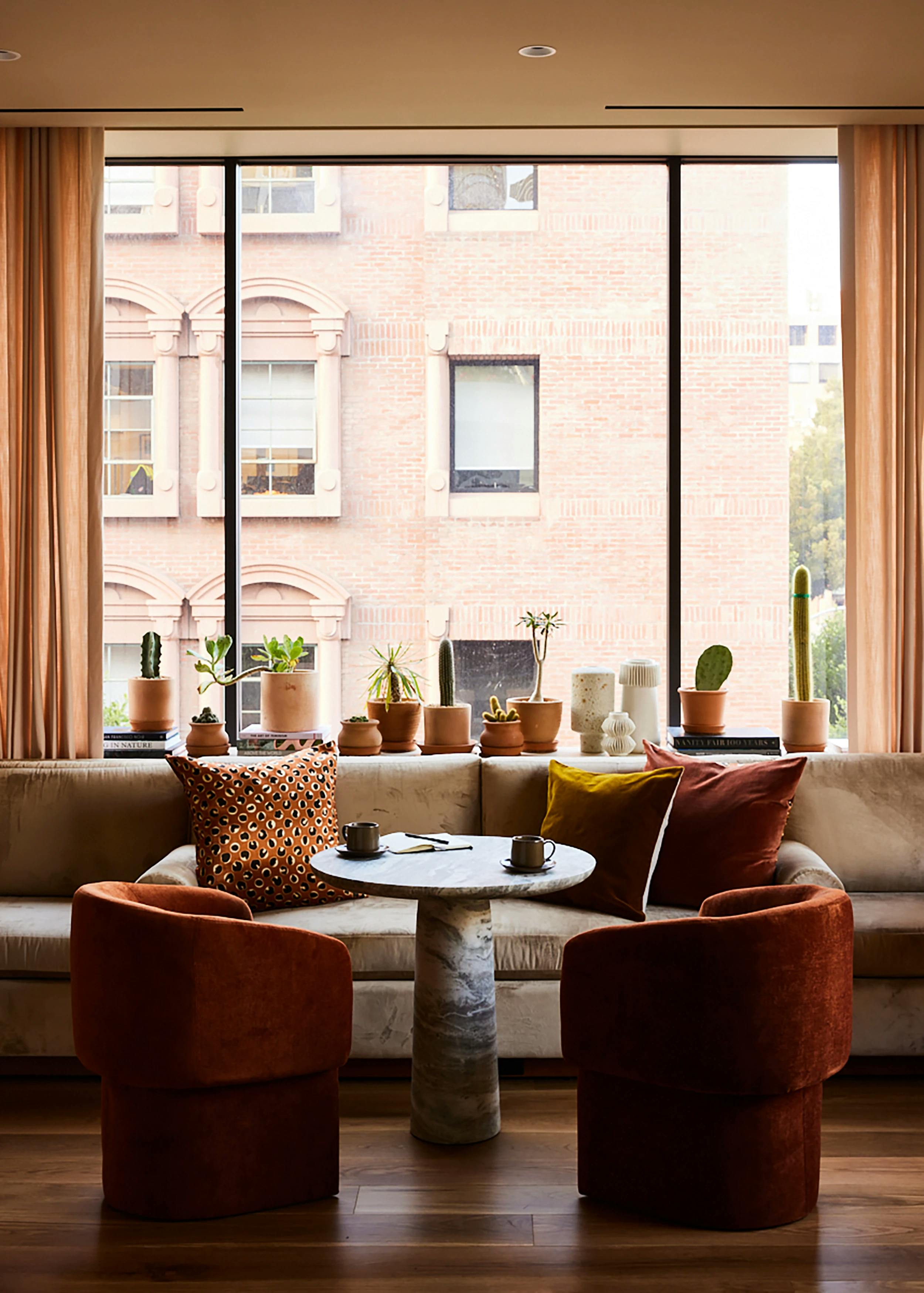 A lounge area at the Chief San Francisco Clubhouse, featuring a sofa and two red armchairs in front of a large window with potted plants on the windowsill.