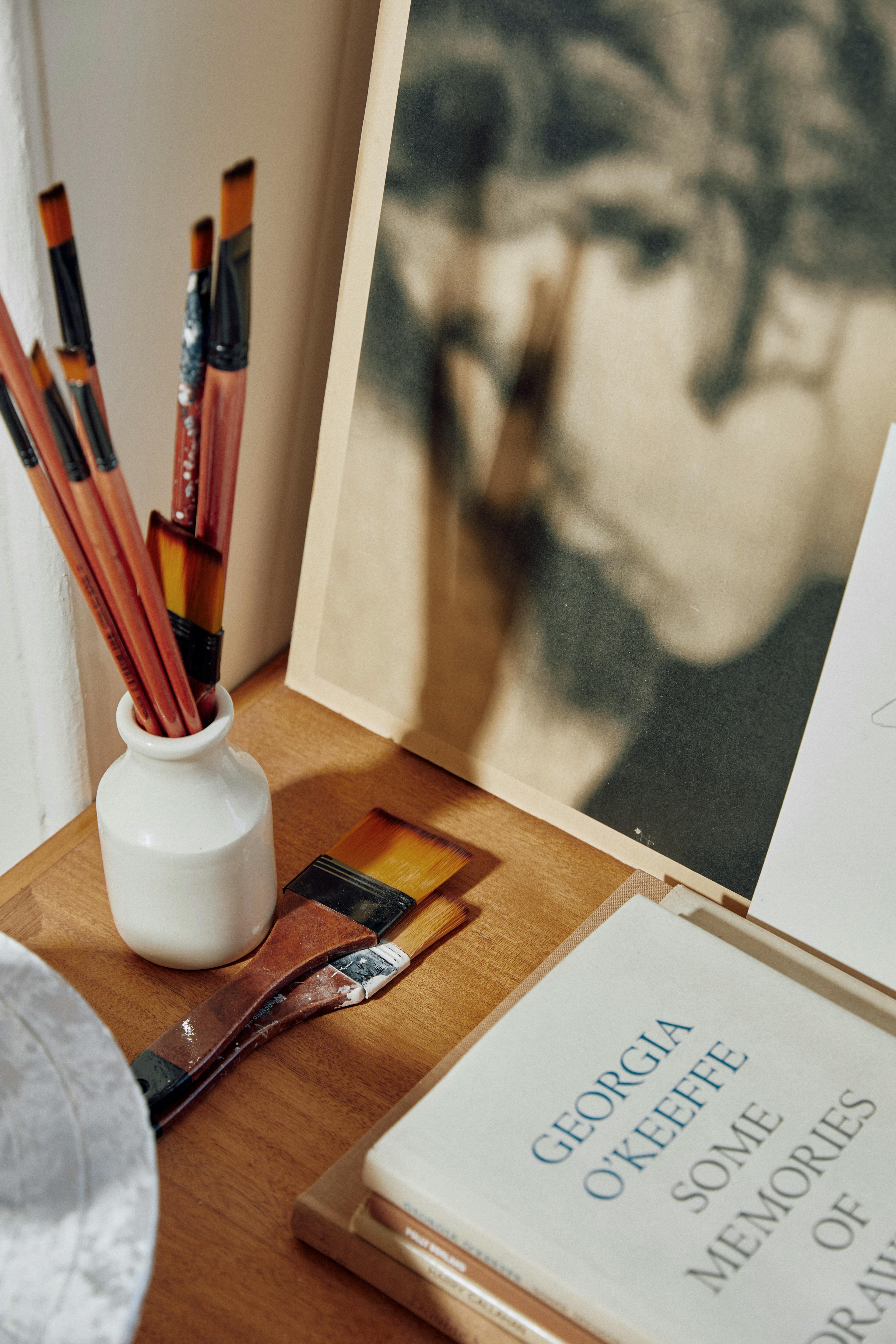 A bottle of brushes and books sits on a wood table at the studio of Caroline Walls.