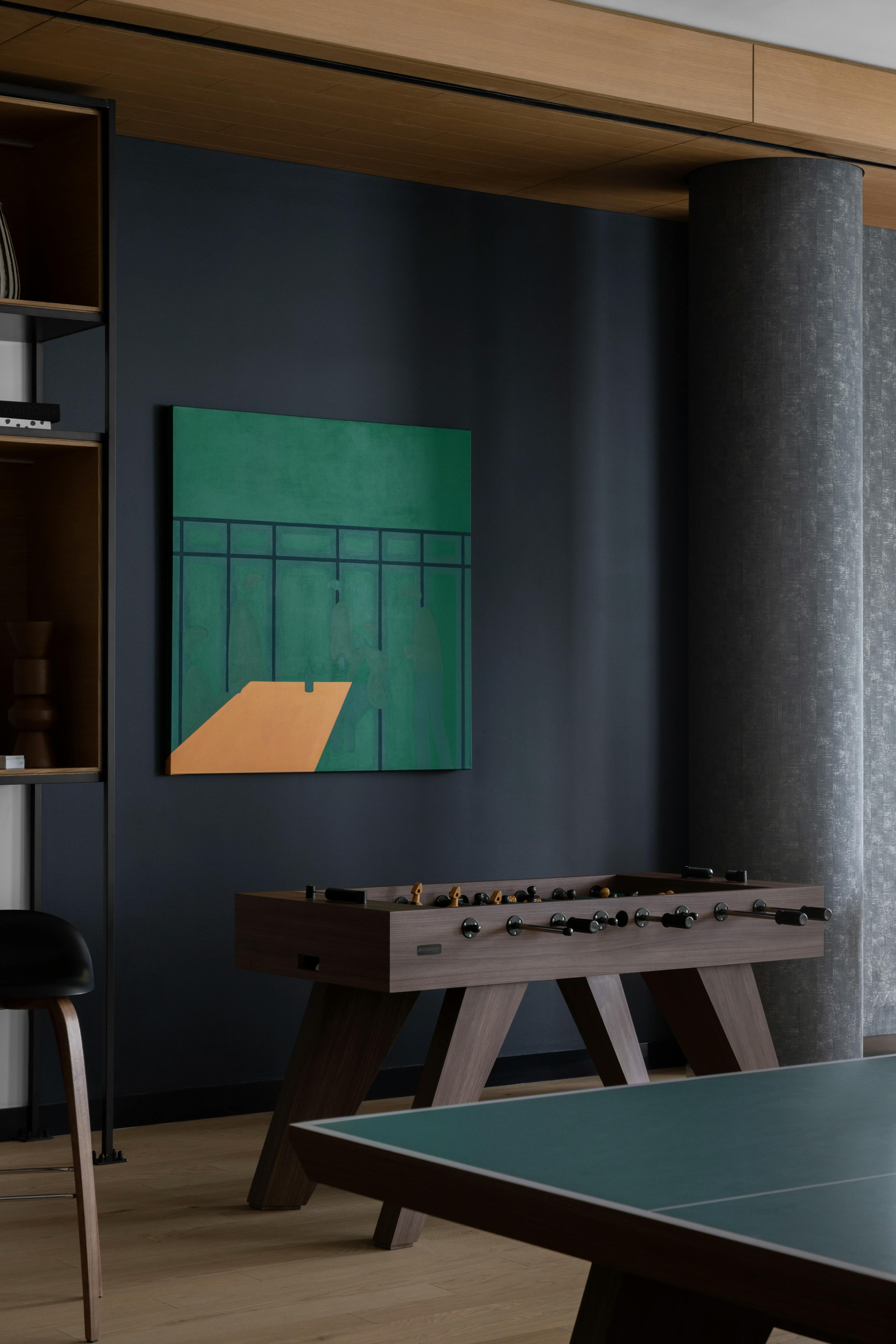 A dark green and orange painting by artist Dana Bell within a game room with a foosball table at Gotham Point.