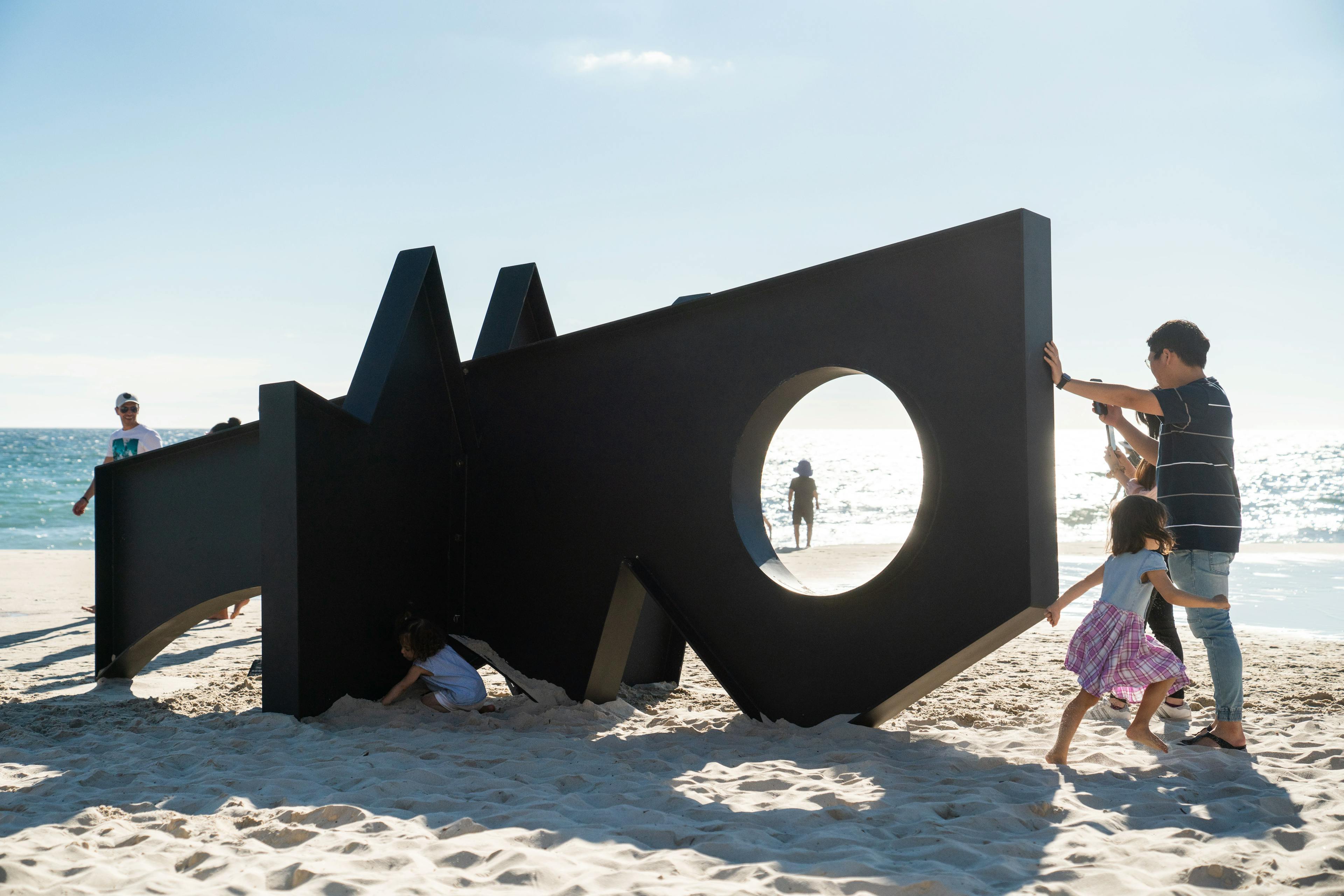 Man and little girl next to an oversized black sculpture by artist Fitzhugh Karol on a beach in Australia.
