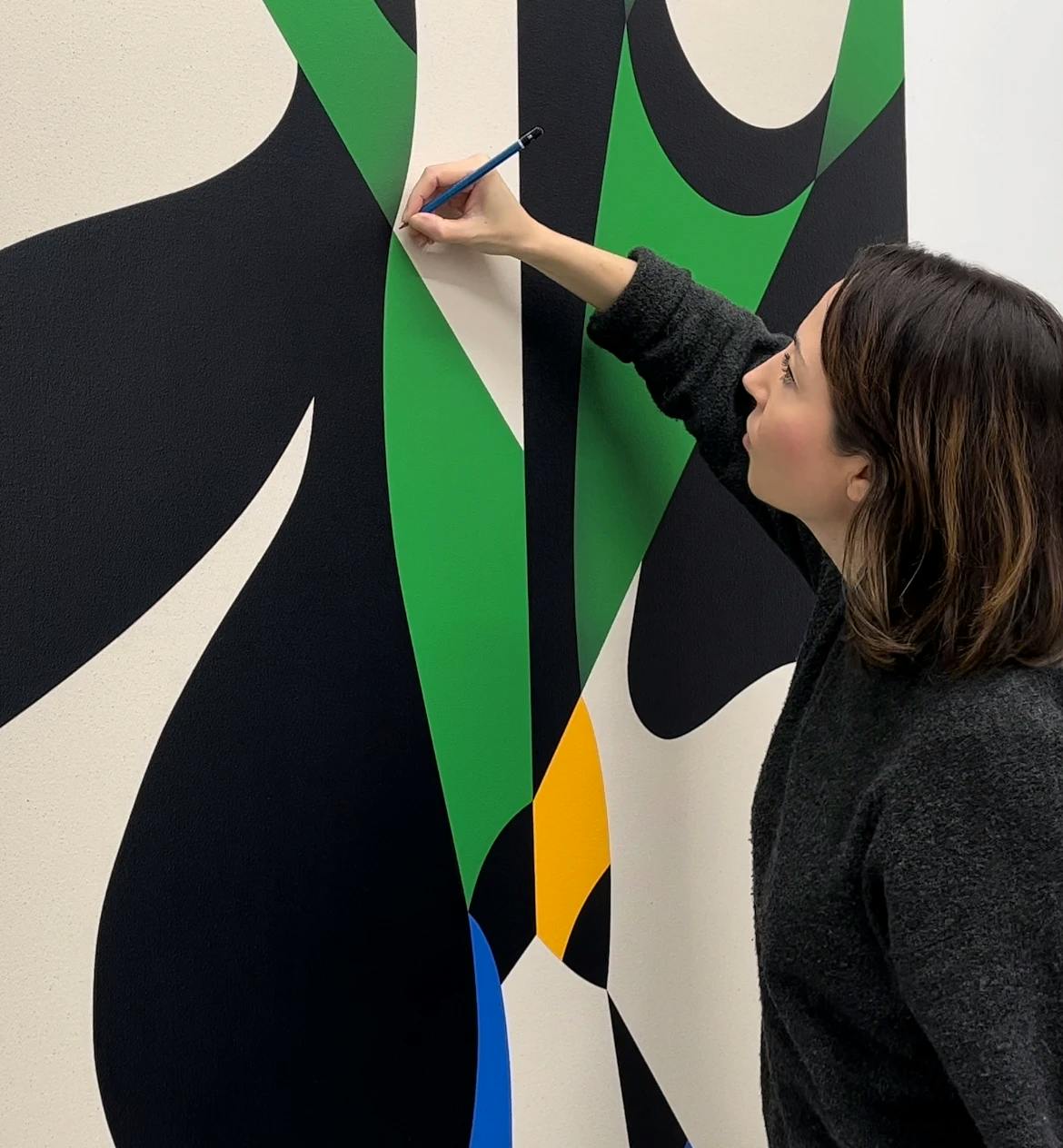 Artist Senem Oezdogan working on a large green, black, yellow, blue and beige painting in her studio. 